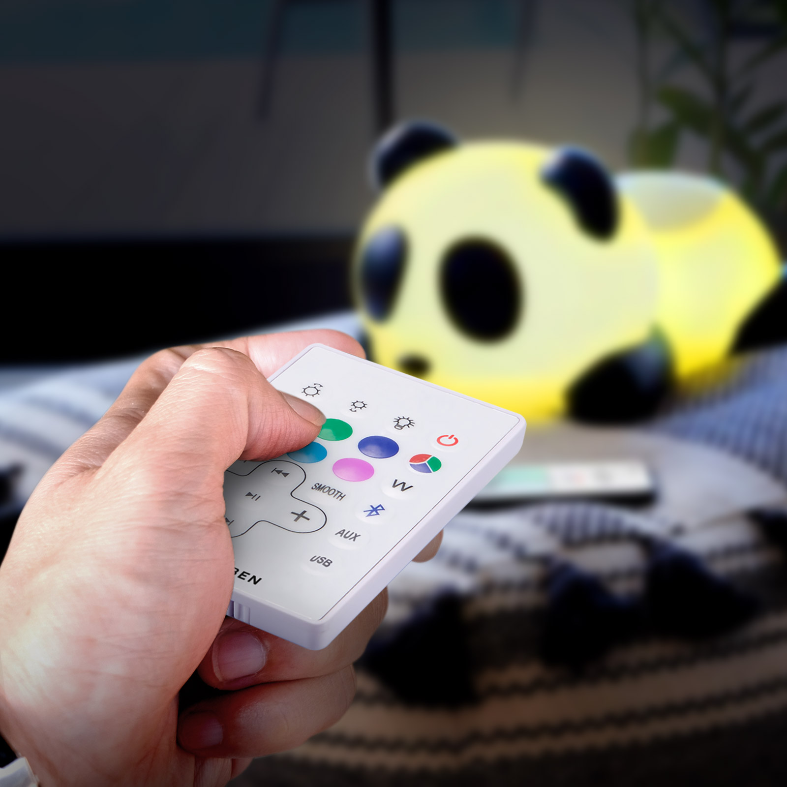 Hand hält eine weiße Fernbedienung mit Tasten, in der Nähe einer gelben Panda-Lampe.