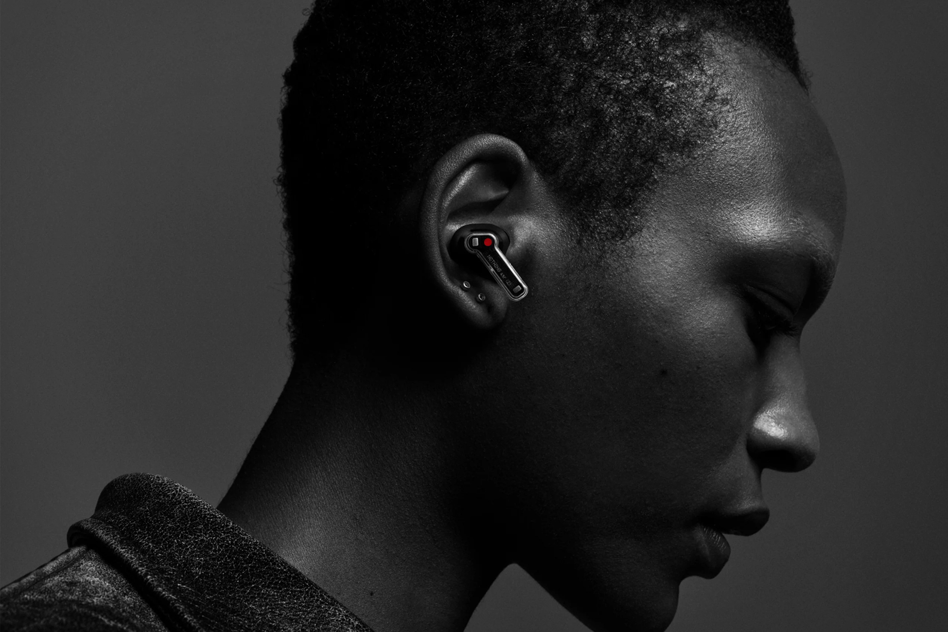 Osoba ze słuchawką w uchu, widok z profilu, czarno-białe, szare tło.