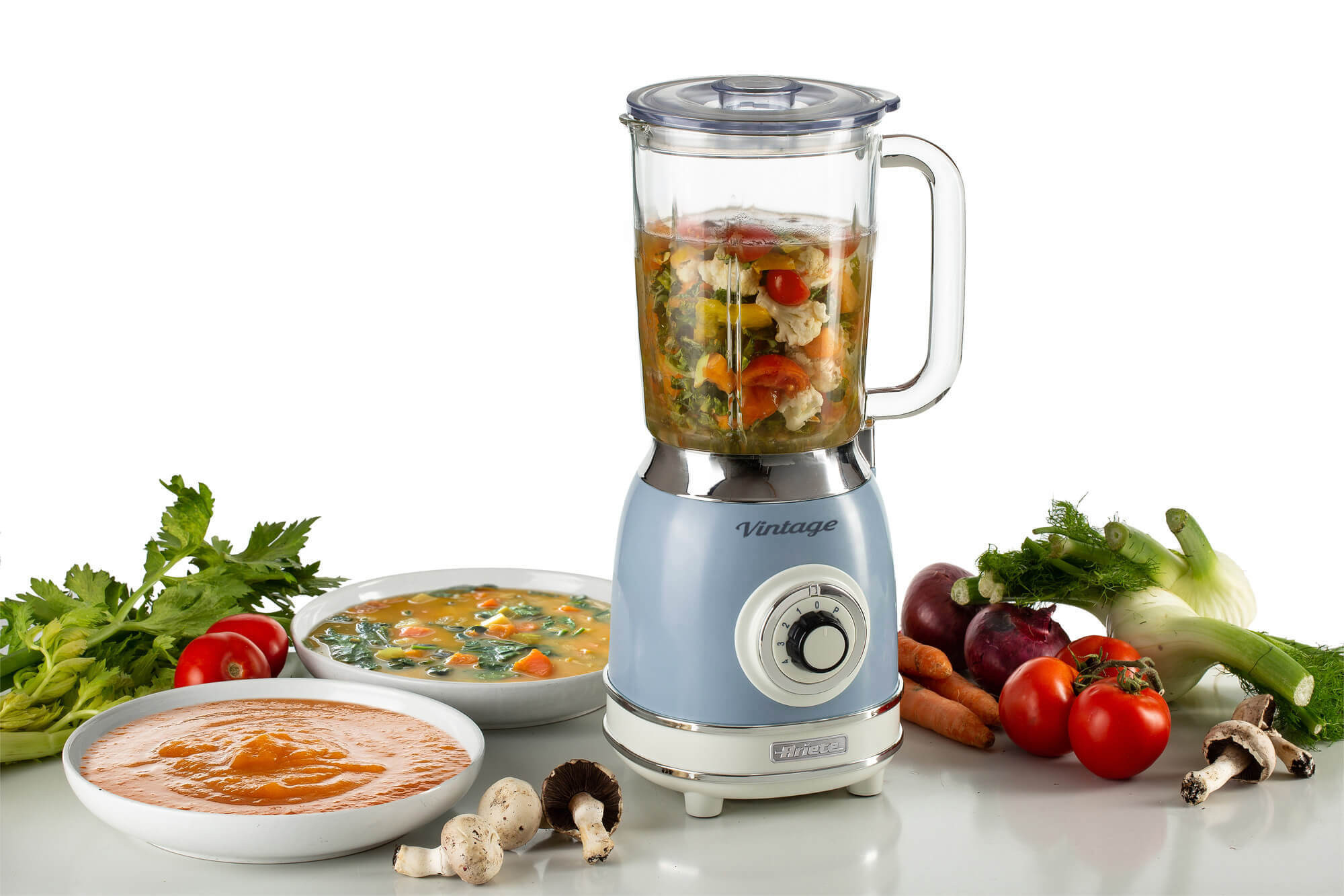 Blauwe Vintage blender met soepkommen en groenten eromheen. Soep zit in de blender.