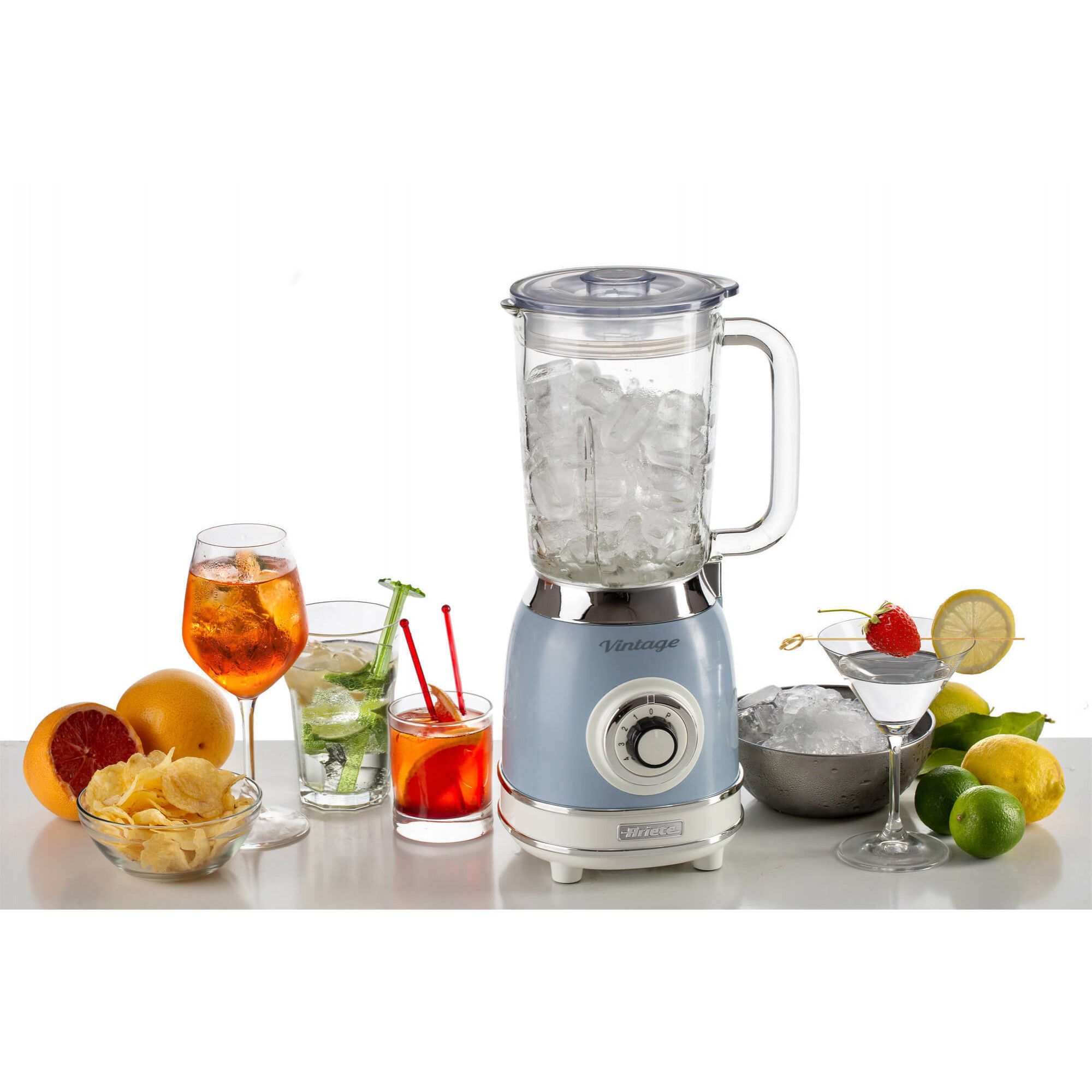 Een blauwe blender met ijs, drankjes, fruit en chips op tafel.