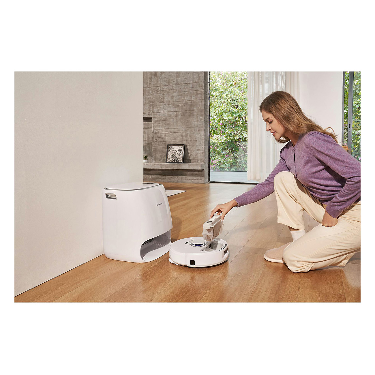 Frau mit Roboter-Staubsauger und Dockingstation. Holzboden. Weiße Wand.