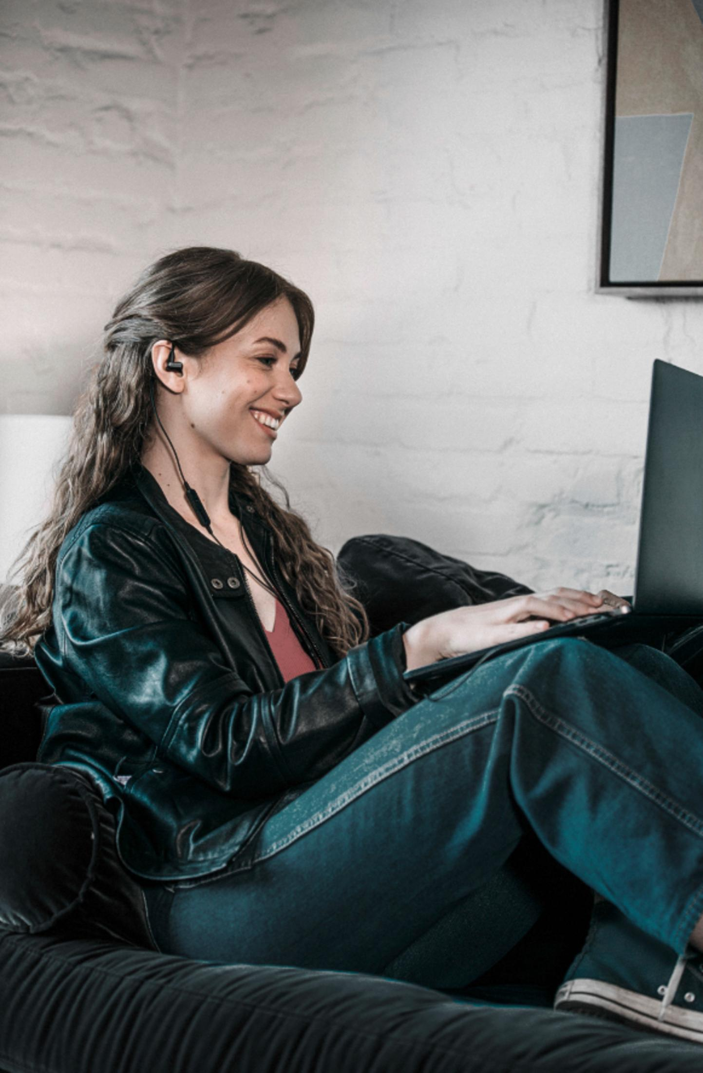Femme avec un casque et utilisant un ordinateur portable. Souriante, dans une pièce. Veste noire.