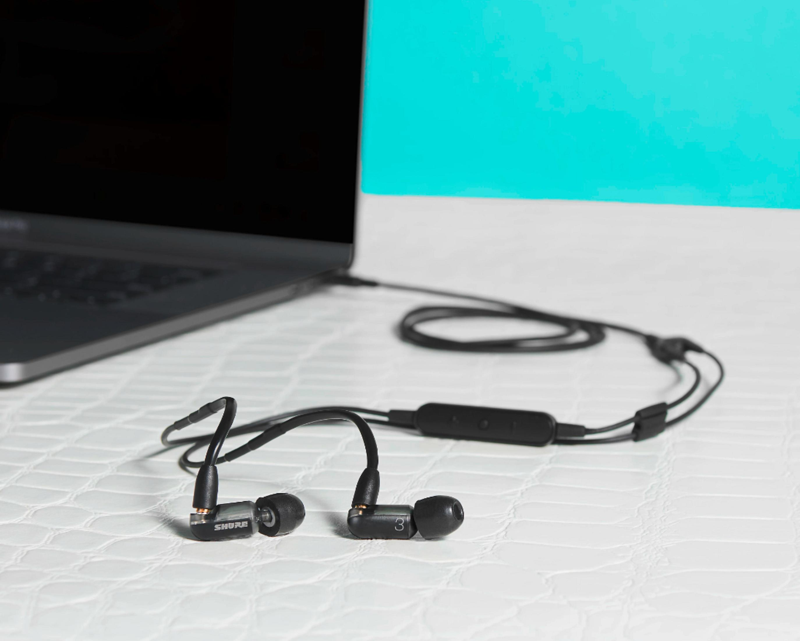 Écouteurs Shure connectés à un ordinateur portable. Les écouteurs sont noirs, le câble est noir, l'ordinateur portable est fermé.