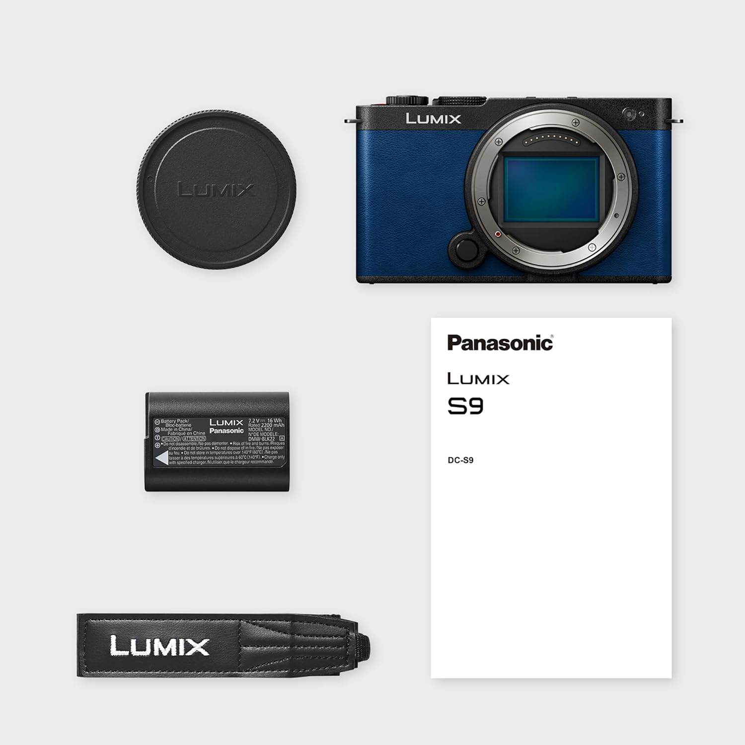 Eine blaue Lumix-Kamera mit Zubehör: Objektivdeckel, Akku, Riemen und Handbuch. Alles auf weißem Untergrund.