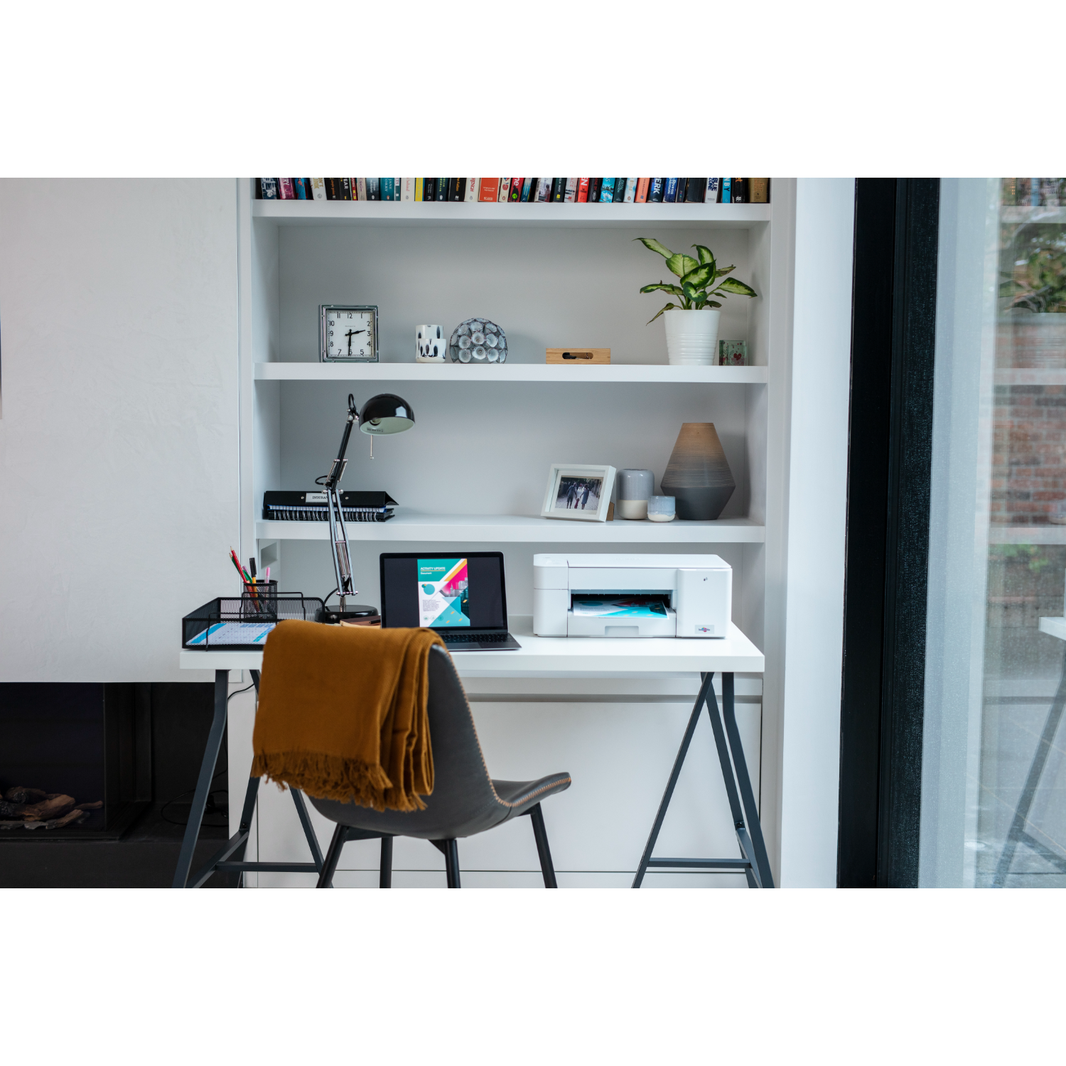 Konfiguracja domowego biura: biurko z laptopem, drukarką, lampą i książkami na półce.