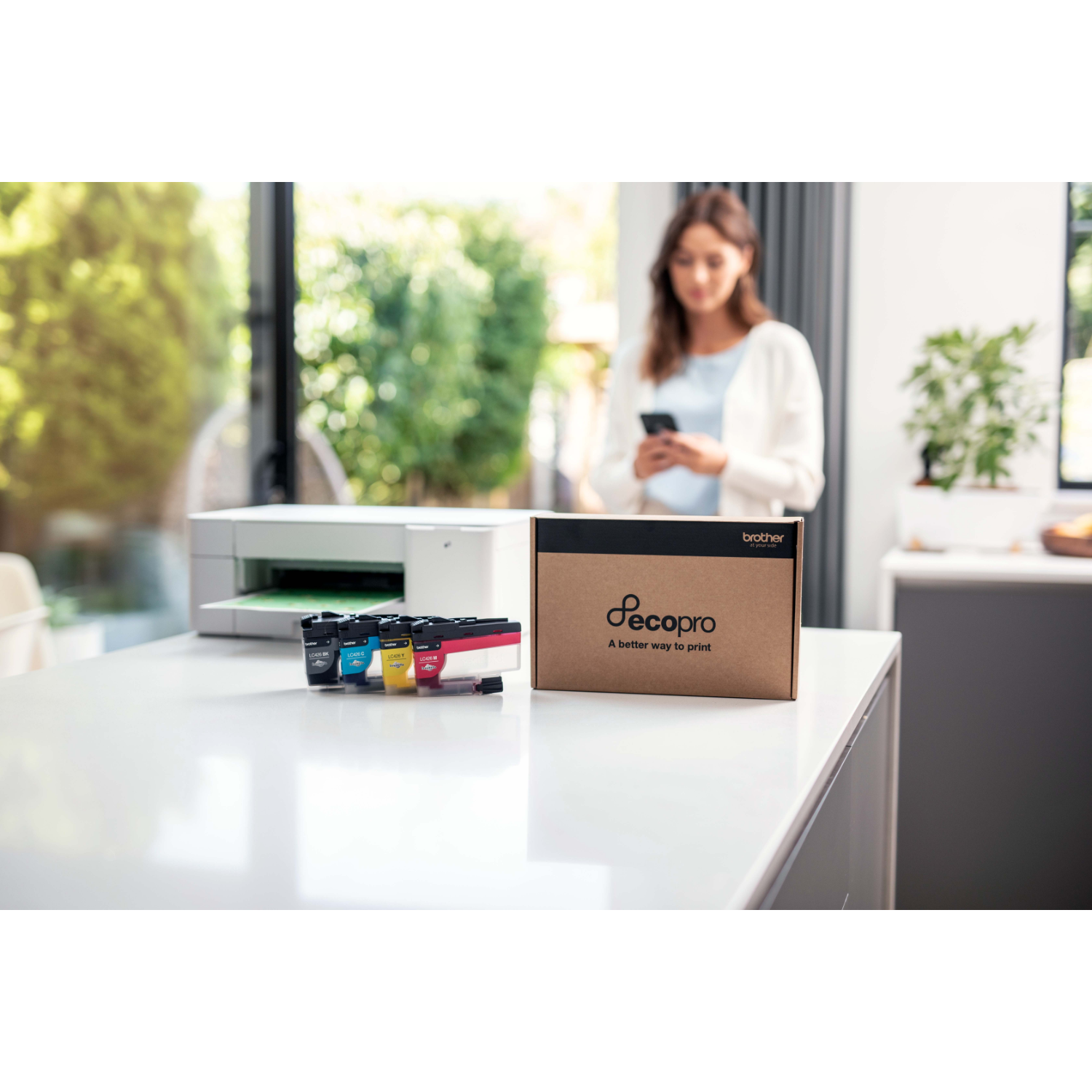 Kobieta w tle, drukarka po lewej, wkłady i pudełko z tuszem na stole.