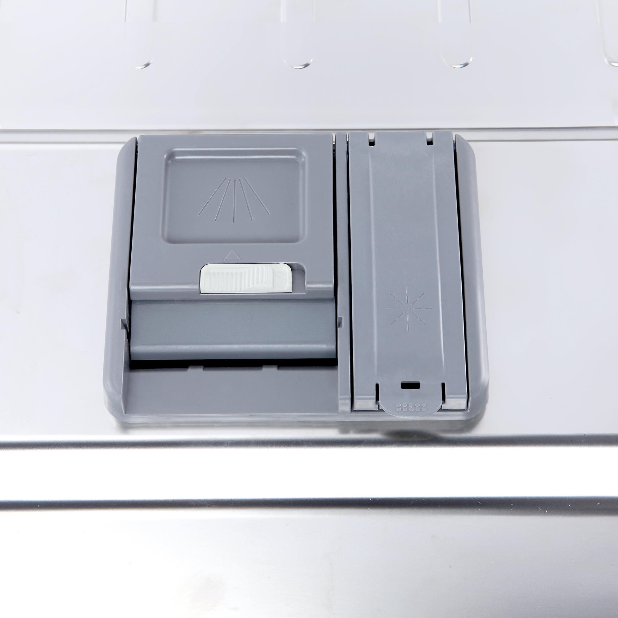 Un primer plano del dispensador de jabón de un lavavajillas. El dispensador es gris y está dentro de un interior de acero inoxidable.