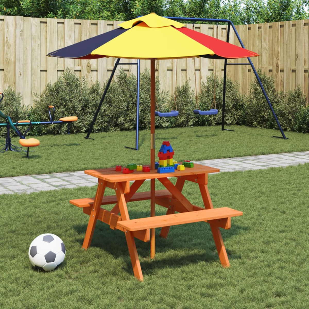 Ein Picknicktisch aus Holz mit Bänken, einem bunten Schirm und Spielzeug auf einer Wiese.