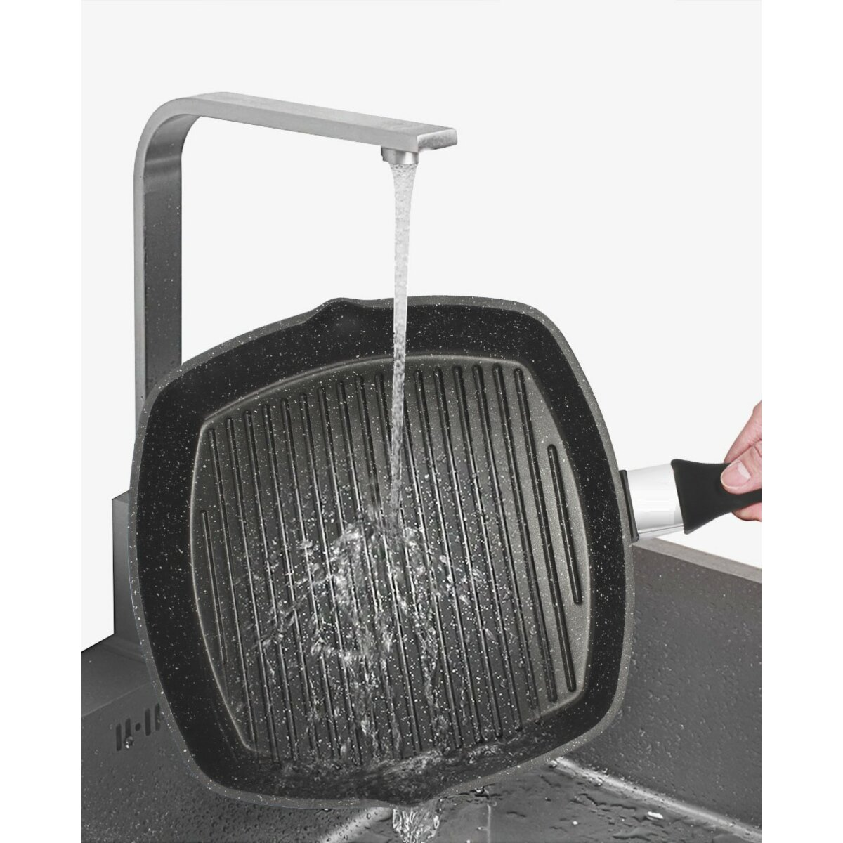 Wasser gießt auf eine schwarze Grillpfanne in einem Waschbecken, weißer Hintergrund.