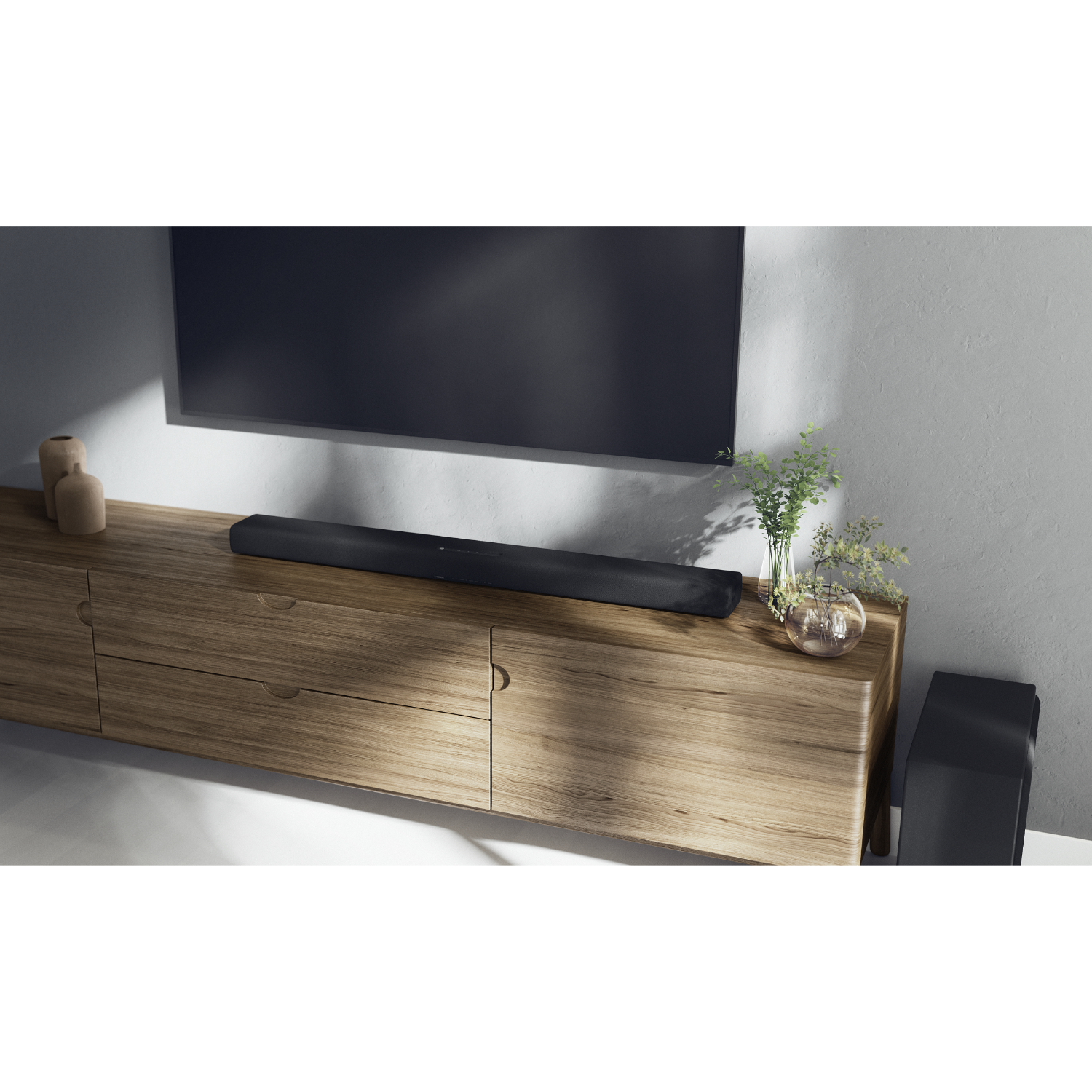 Schwarze Soundbar auf einem Holzschrank unter einem Fernseher. Pflanzen und Subwoofer sichtbar.