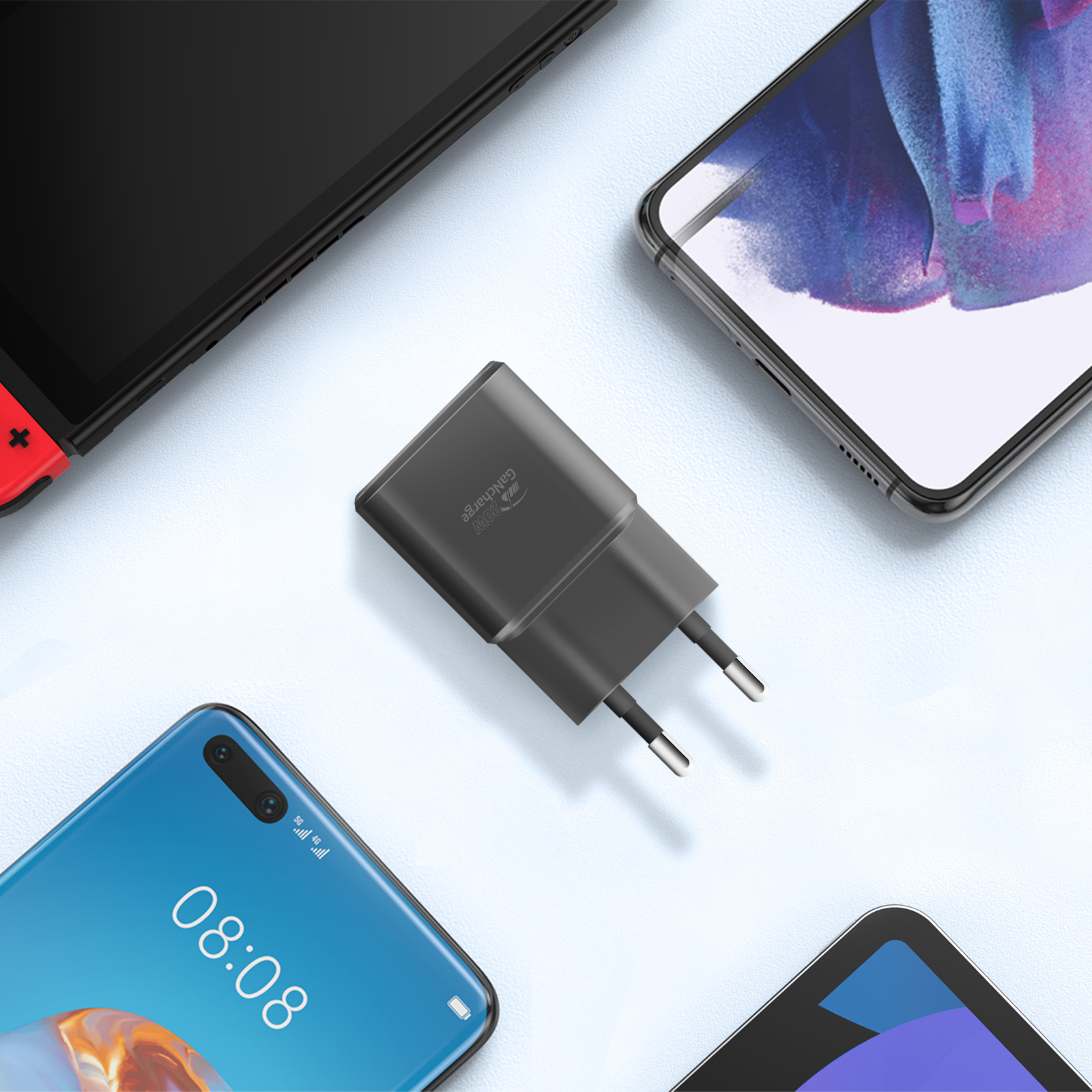 Un caricabatterie grigio con due pin, circondato da telefoni e una console di gioco.