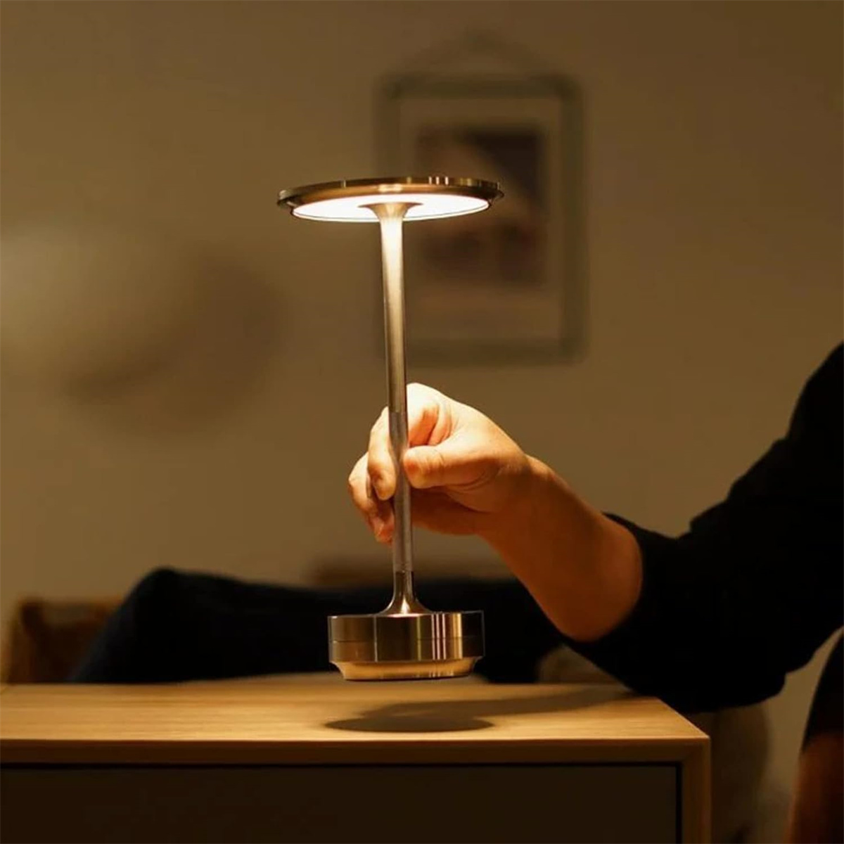 Hand hält eine moderne, metallische Lampe mit rundem Kopf, vor dunklem Hintergrund.