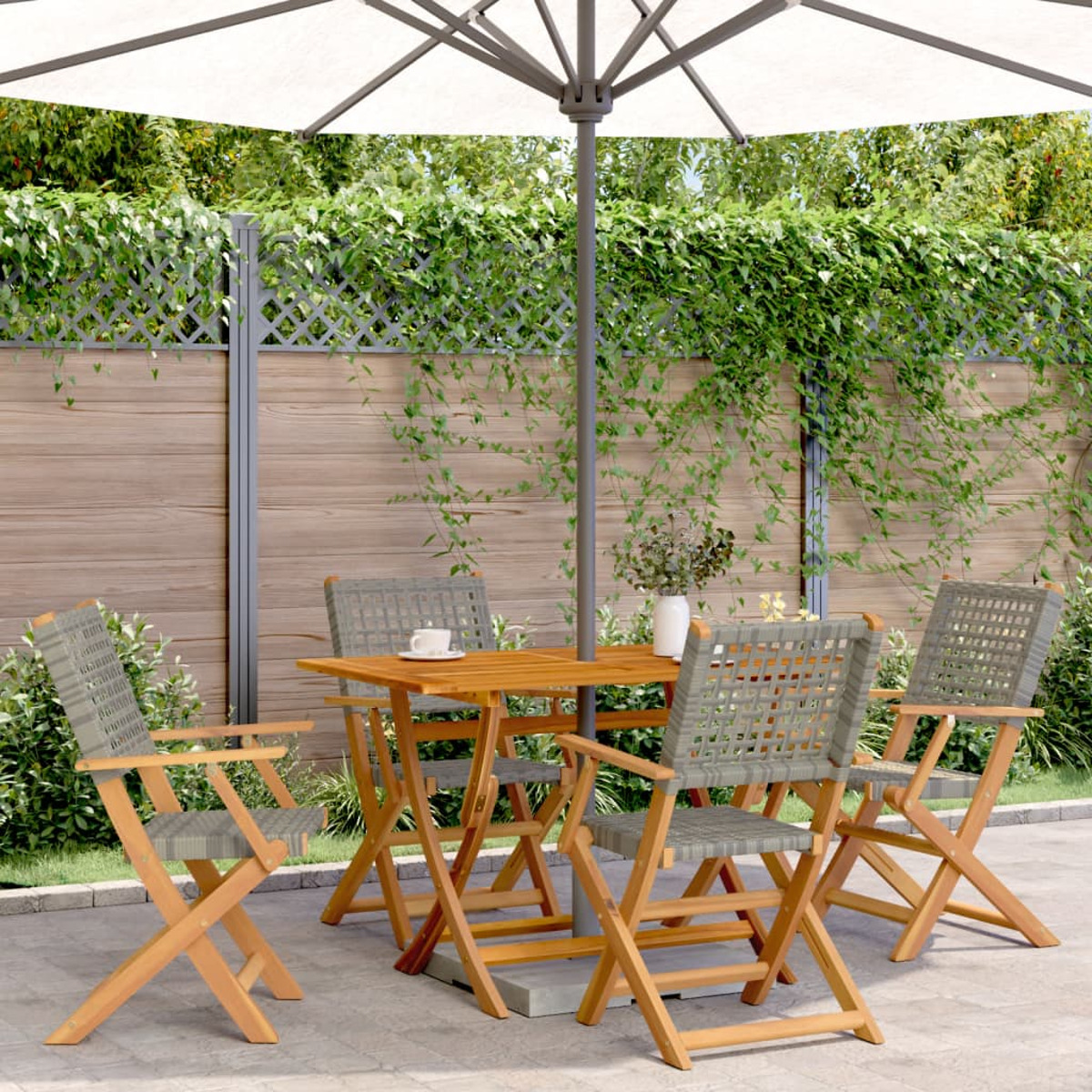 Un set da patio con un tavolo in legno, quattro sedie e un ombrello bianco. Le sedie hanno sedute grigie intrecciate.