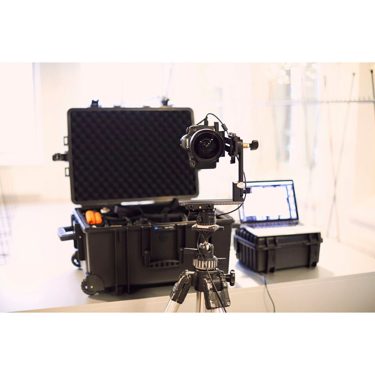 Ein Foto-Setup mit Kamera, Stativ, Koffer und Laptop in einem weißen Raum.