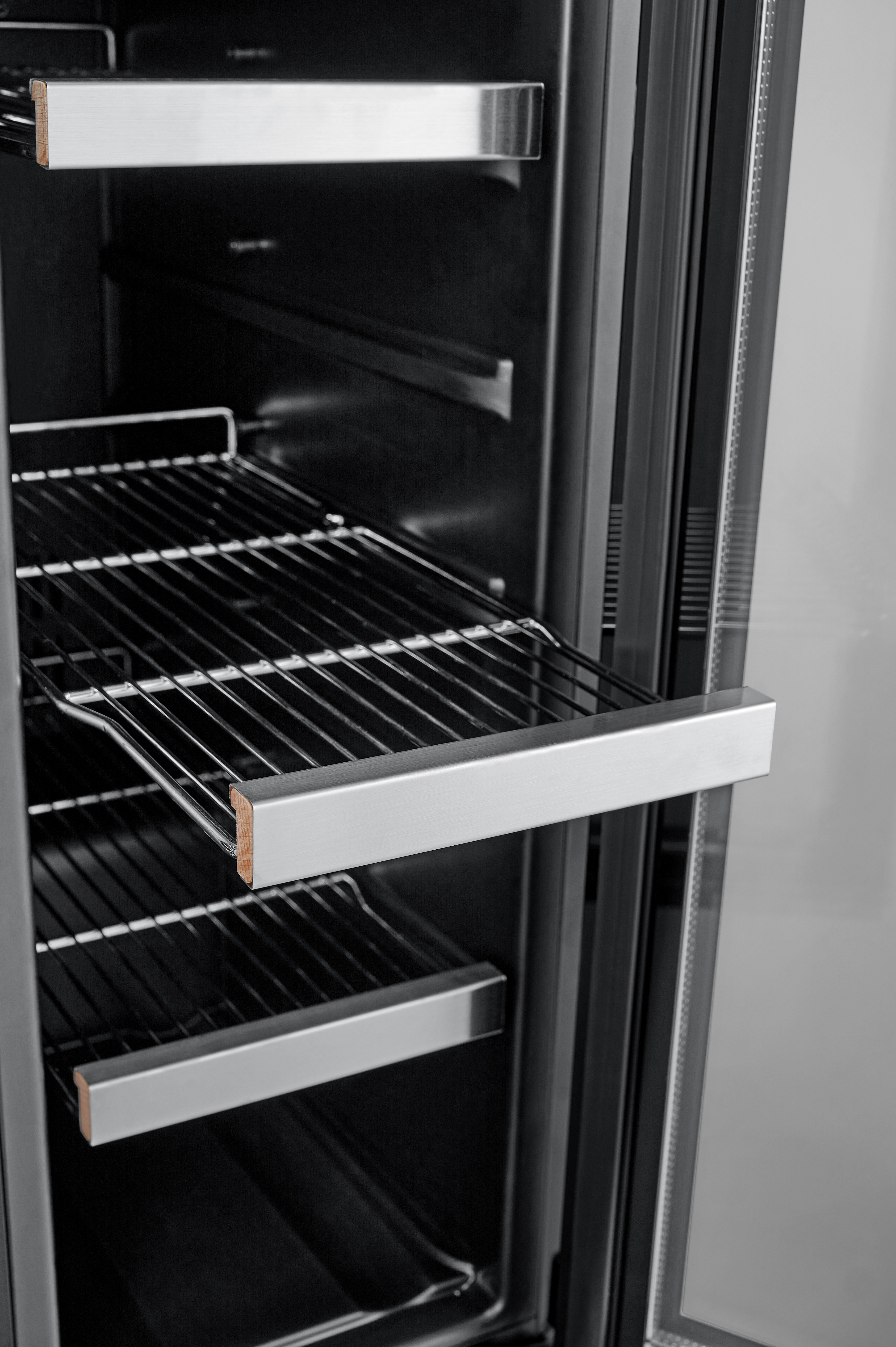 Ein offener Kühlschrank aus Edelstahl mit Drahtregalen im Inneren.