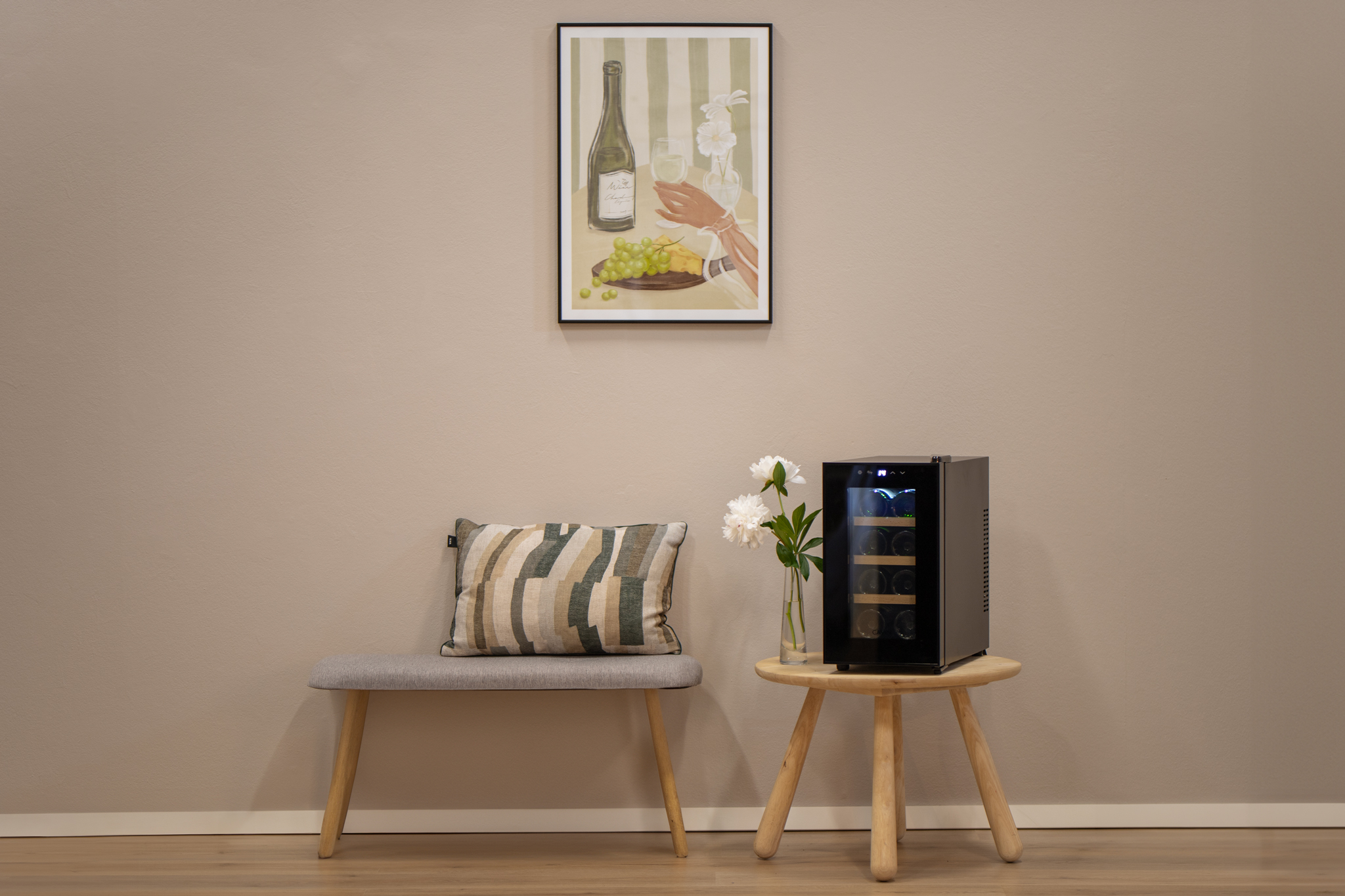 Ein Gemälde über einer Bank mit Kissen, einer Blumenvase und einem Weinkühler.