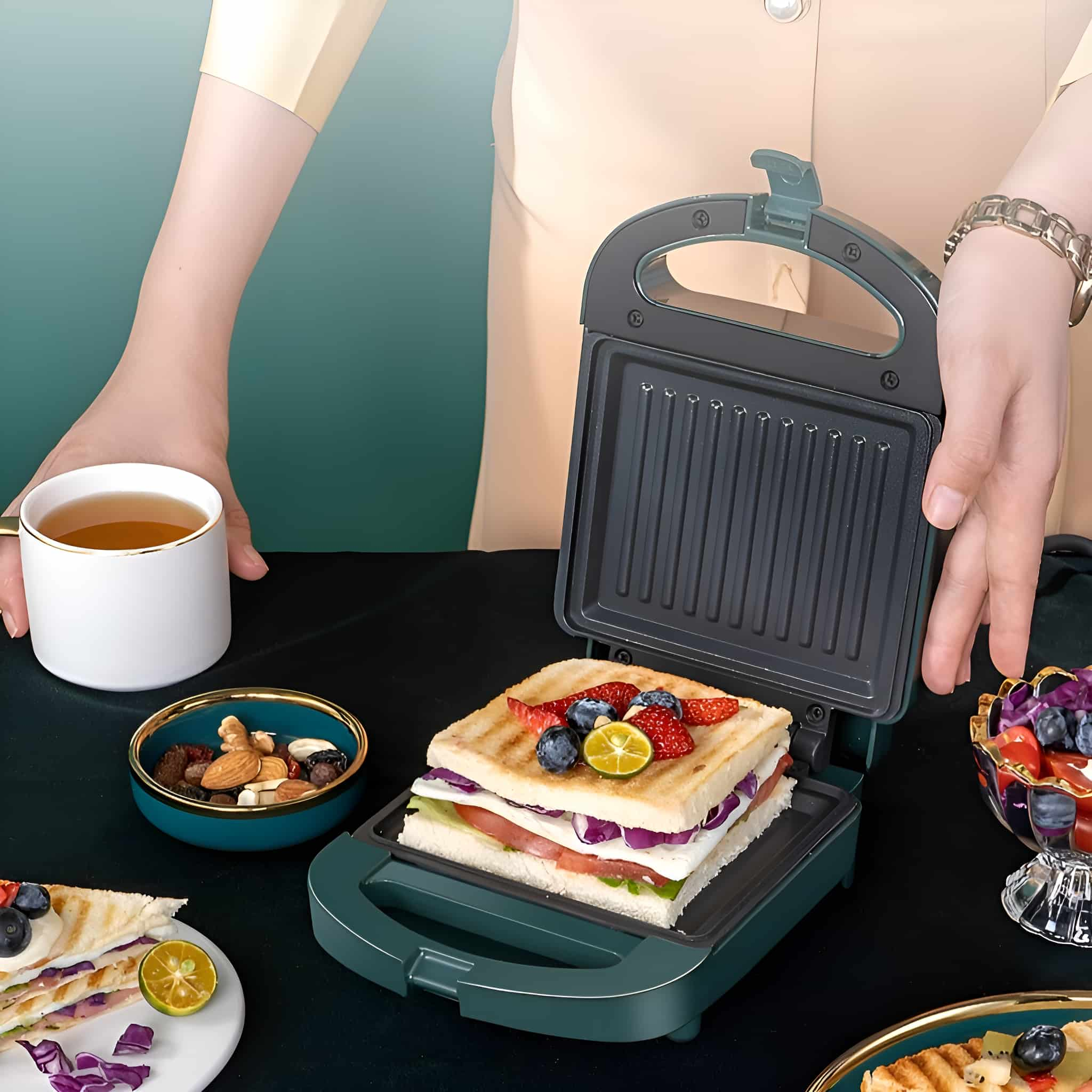 Ein Sandwichmaker mit einem Sandwich darin. Das Sandwich hat Tomaten, Salat und Beeren. Eine Person ist in der Nähe.