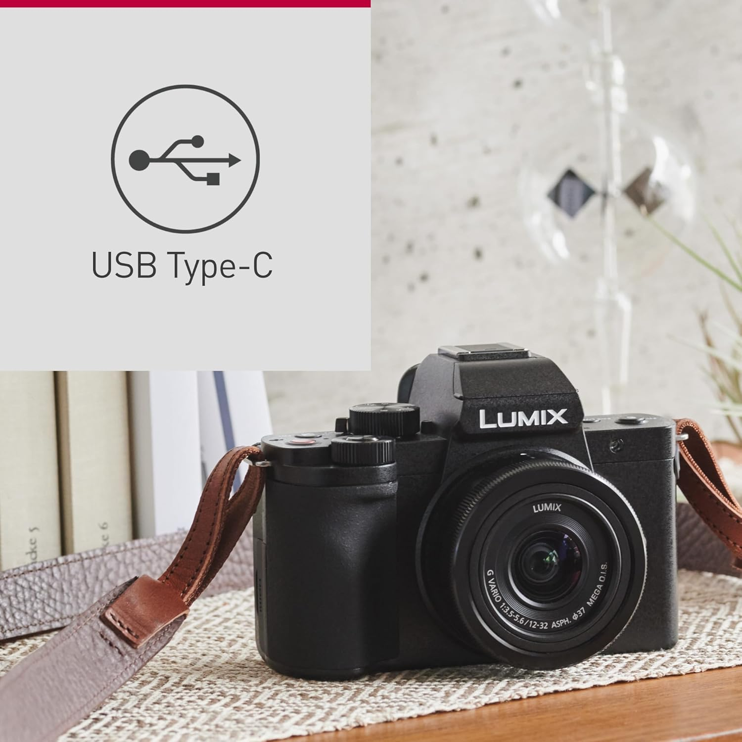 Eine schwarze Lumix Kamera mit braunem Riemen, USB Typ-C Symbol und Büchern im Hintergrund.