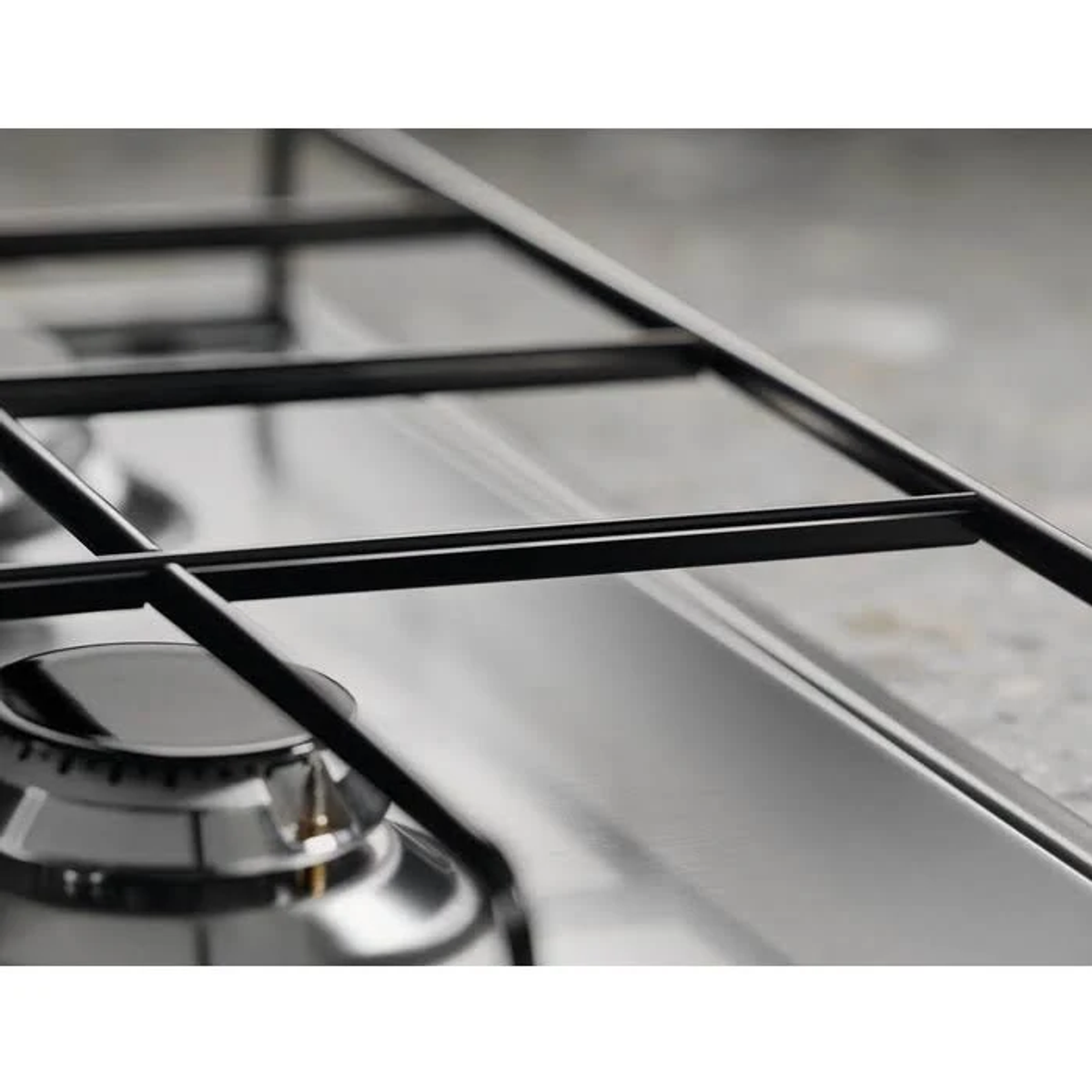 Zbliżenie palnika kuchenki gazowej ze stali nierdzewnej z czarnymi kratkami.