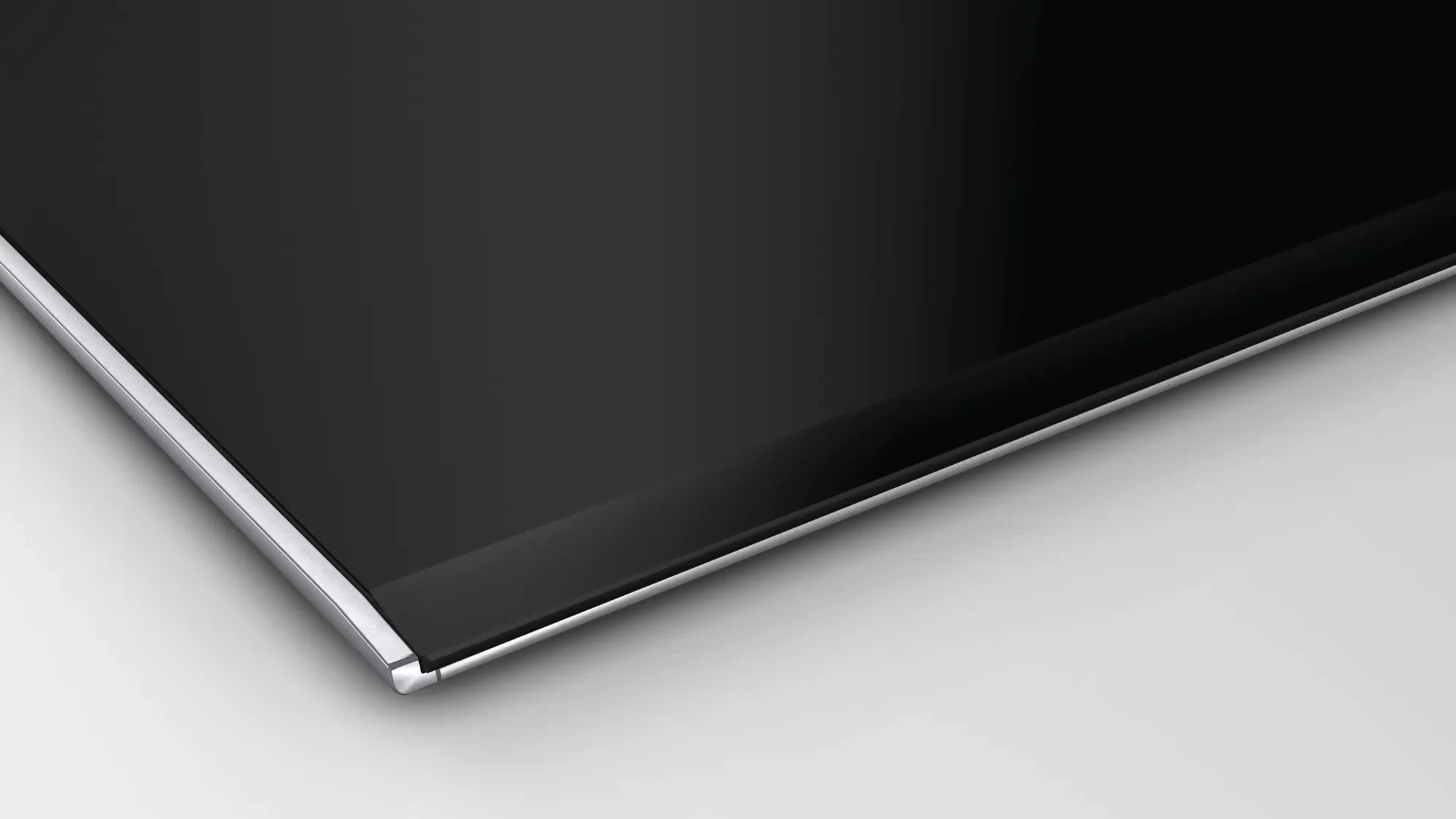 Gros plan sur une table de cuisson à induction noire avec un bord argenté. Elle a une surface élégante et brillante.