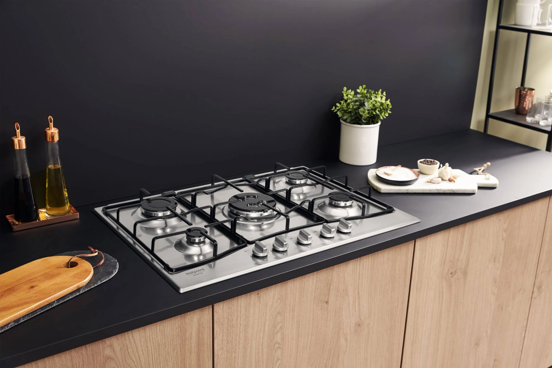 Nowoczesna kuchnia ze stalową płytą gazową, czarnym blatem, drewnianymi szafkami i elementami dekoracyjnymi.