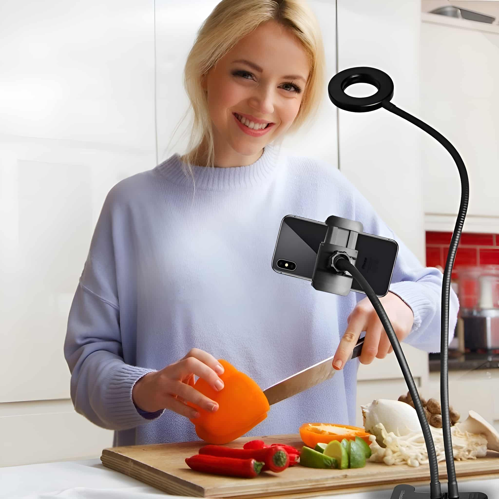 Eine lächelnde Frau schneidet eine Paprika. Sie benutzt einen flexiblen Telefonständer mit Ringlicht.