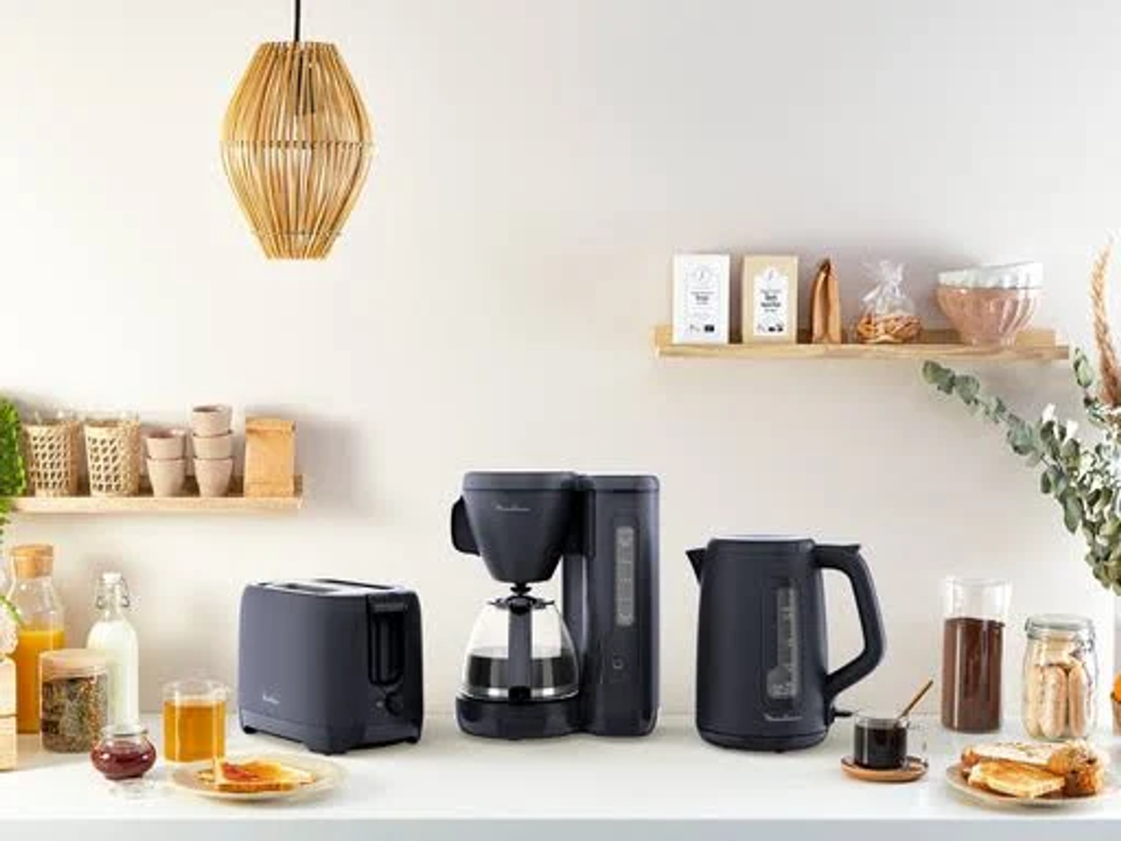 Kitchen scene with appliances. Toaster, coffee maker, kettle, and food items on a white counter.