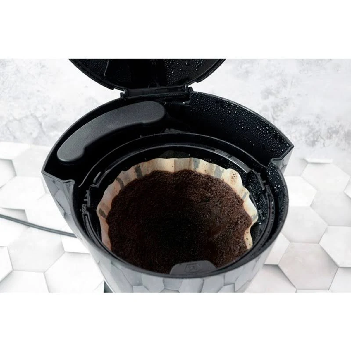 Filtro de cafetera con posos de café. La parte superior está abierta, mostrando el filtro y posos.