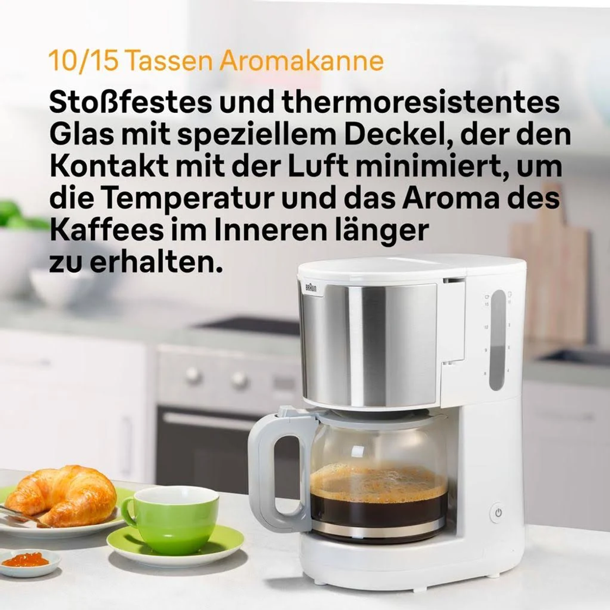 Ekspres do kawy z tekstem. Biały i srebrny. Szklany dzbanek z kawą. Filiżanka i rogalik obok.