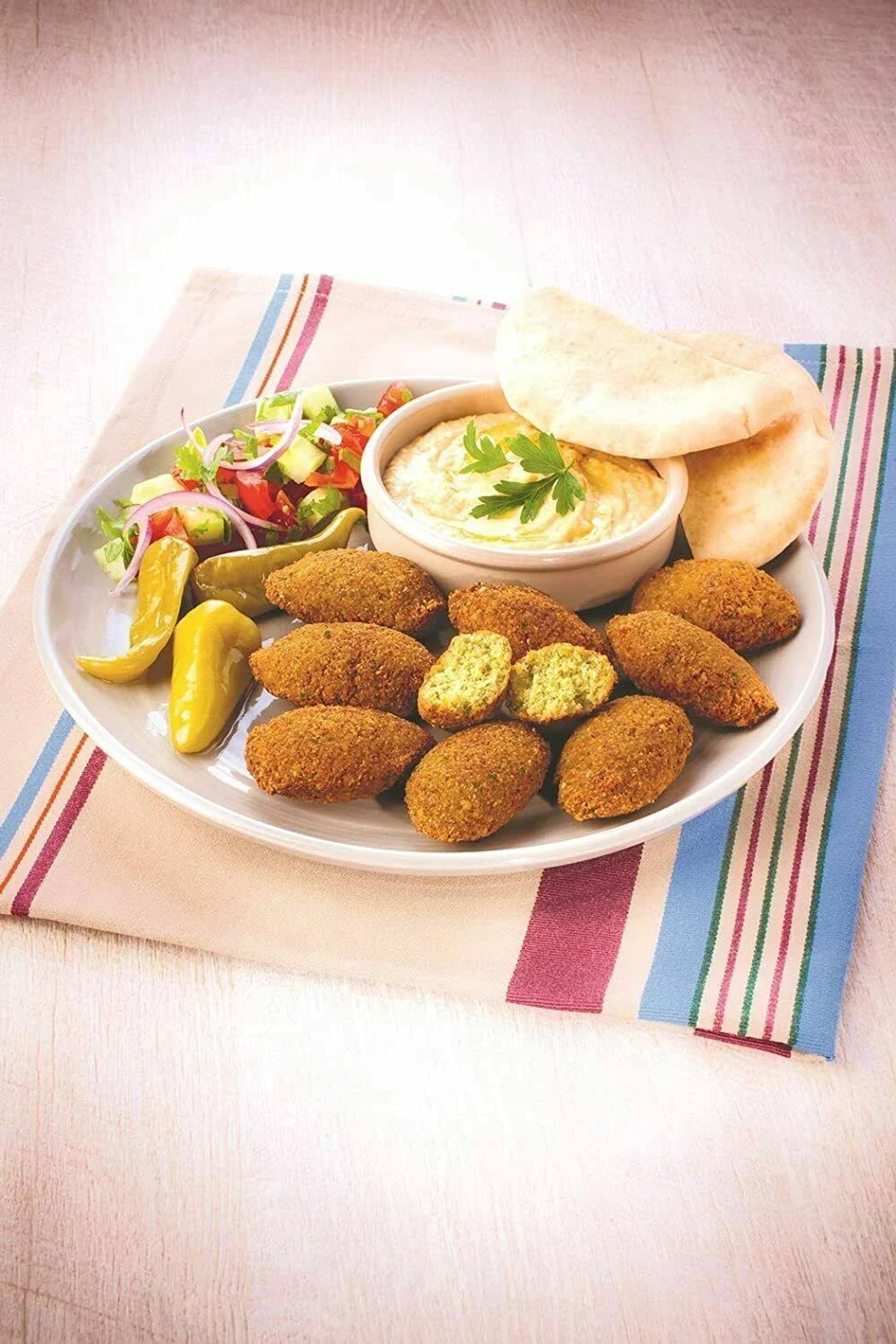Falafel-Teller mit Hummus, Salat, Gurken und Fladenbrot. Gestreifte Serviette.