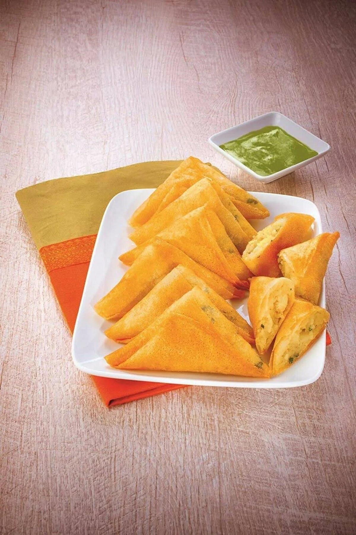 Ein Teller mit Samosas und einer grünen Dip-Sauce. Samosas sind dreieckig und goldbraun.