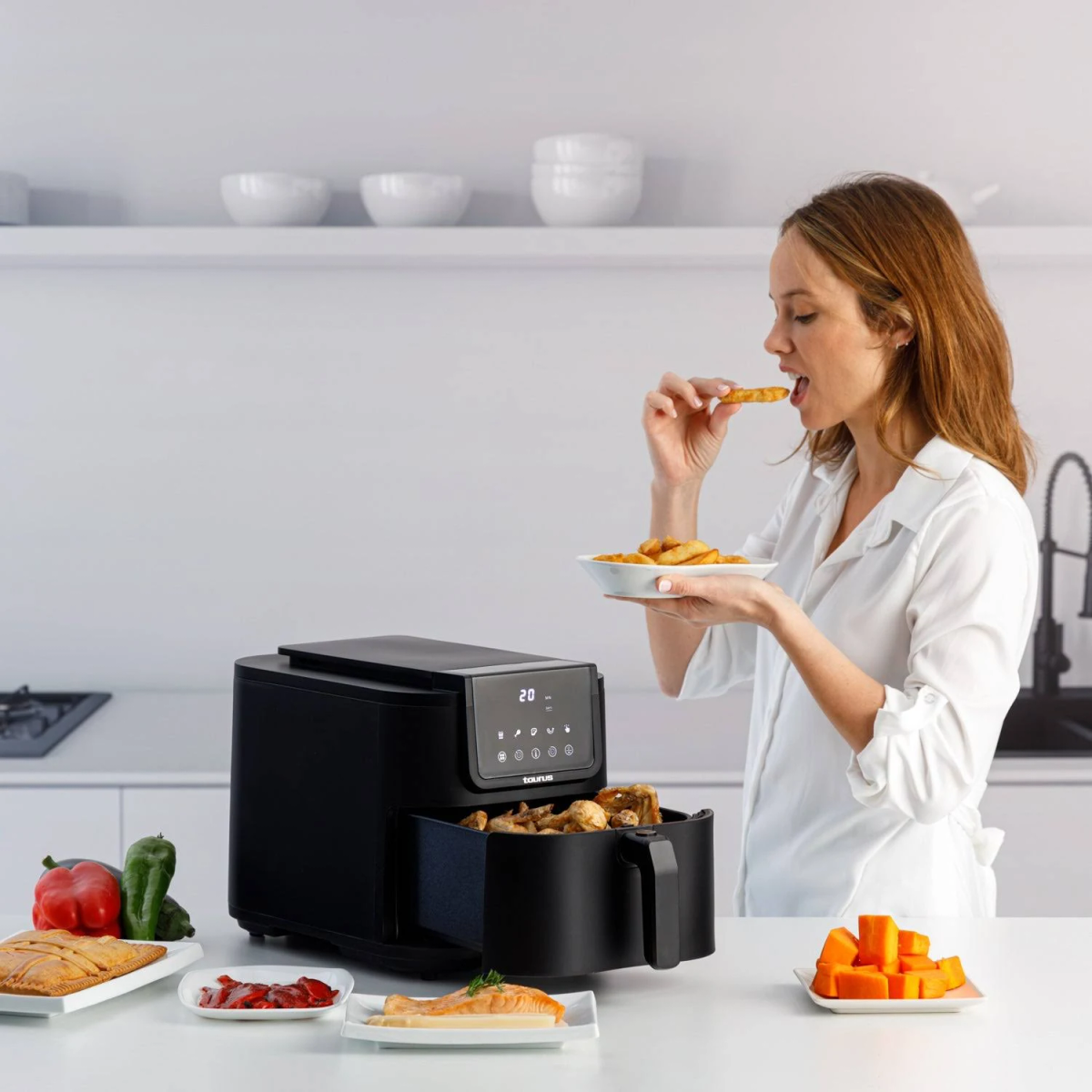 Kobieta je frytki, z frytownicą i warzywami na blacie.