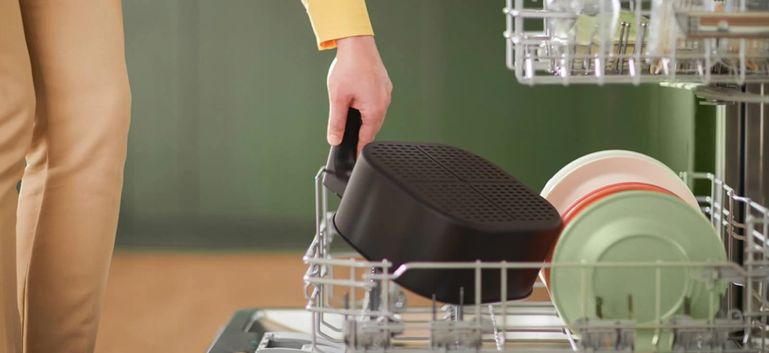 Osoba umieszcza kosz frytkownicy powietrznej w koszu zmywarki. Zielone i różowe talerze również w koszu.