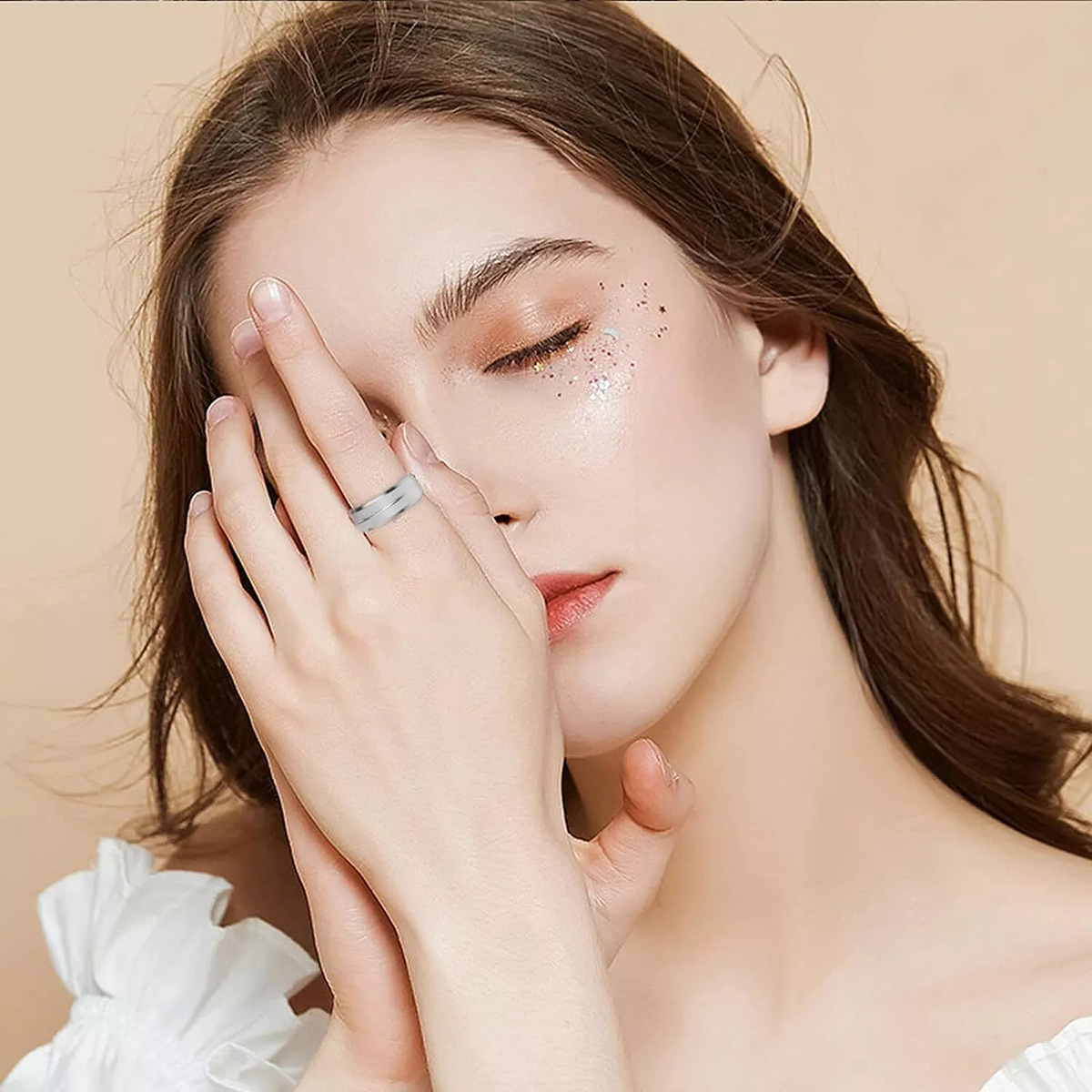 Una mujer está sosteniendo sus manos. Un anillo plateado en el dedo anular de la mano derecha. El fondo es beige.