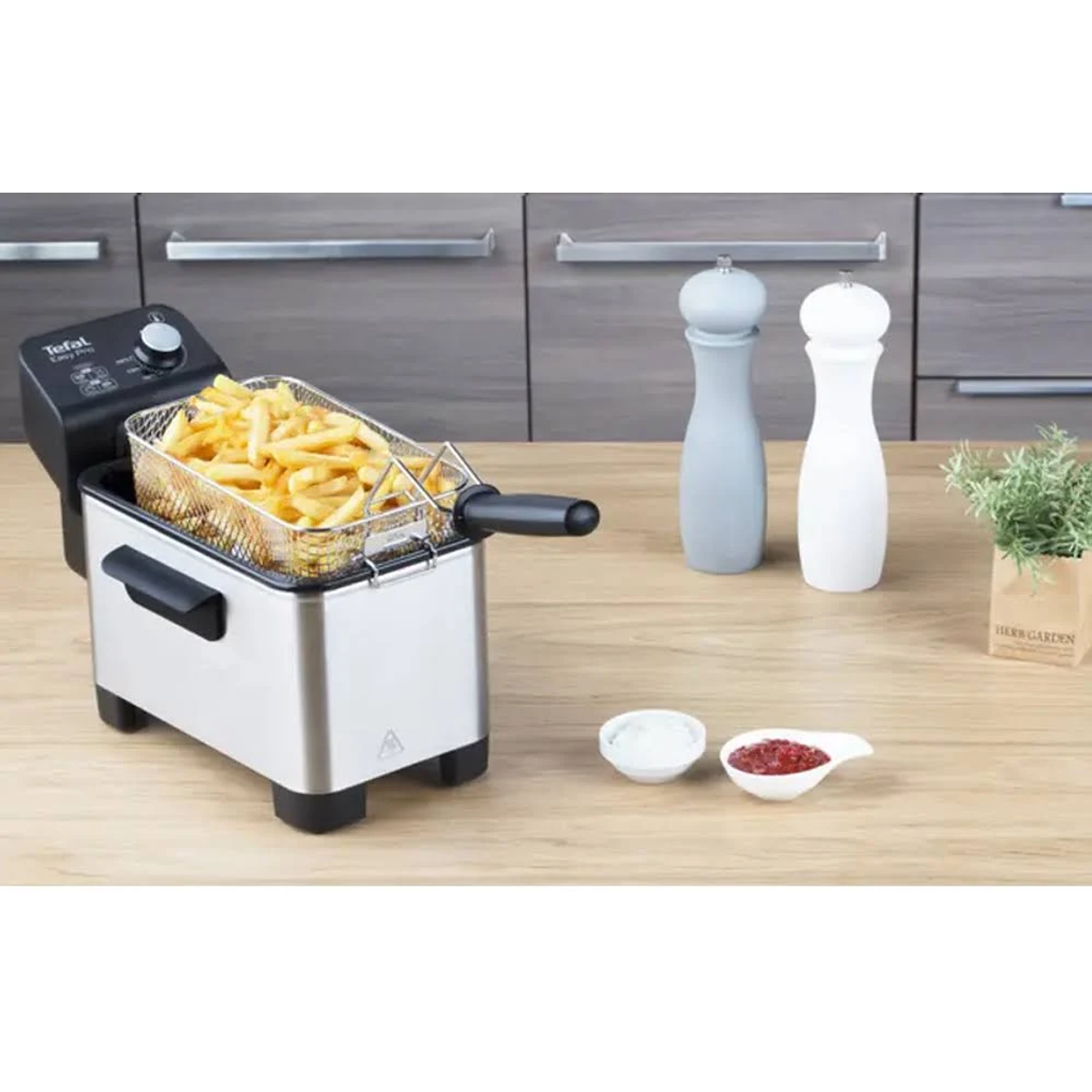 Una freidora con papas fritas, dos saleros y condimentos sobre una superficie de madera.