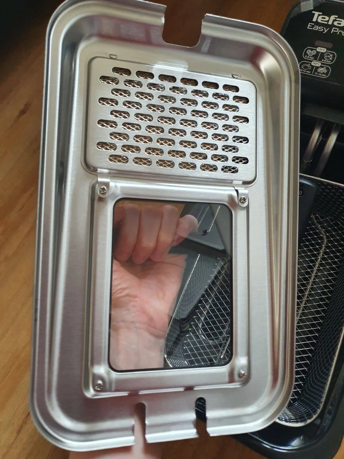 Tapa metálica de freidora de aire con malla y mano visible a través de la apertura.