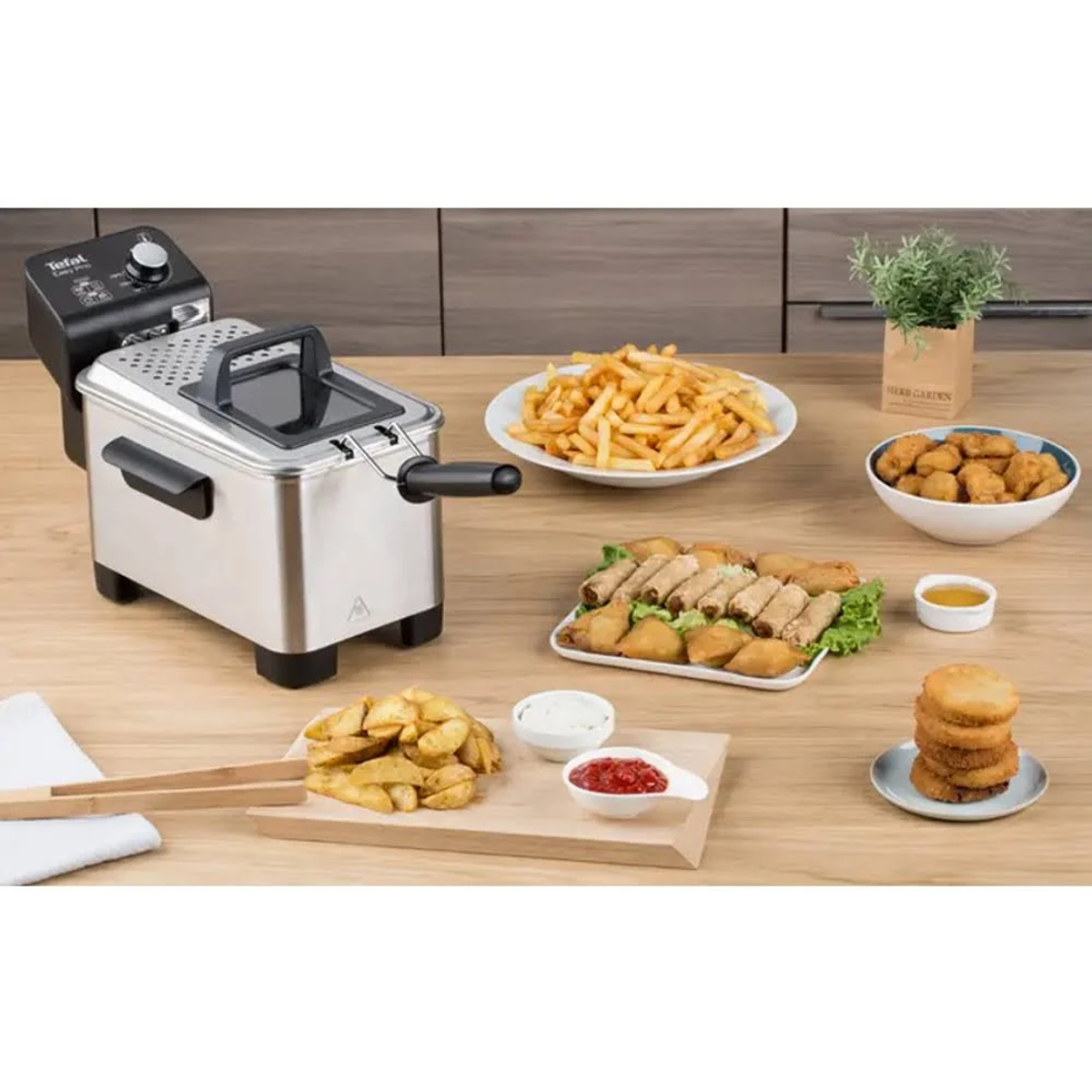 Una mesa con comida frita, una freidora y salsas. Incluye patatas fritas, pollo y más.