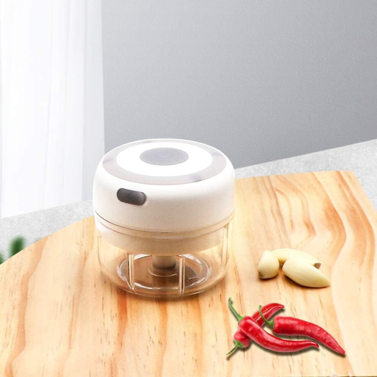 Mini picadora de alimentos blanca y gris sobre tabla de madera con ajo y pimientos rojos.