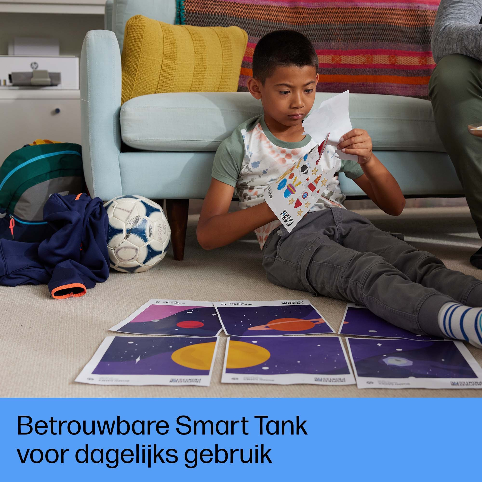 Chłopiec na podłodze bawi się kartami. Piłka nożna po lewej. W tle sofa.