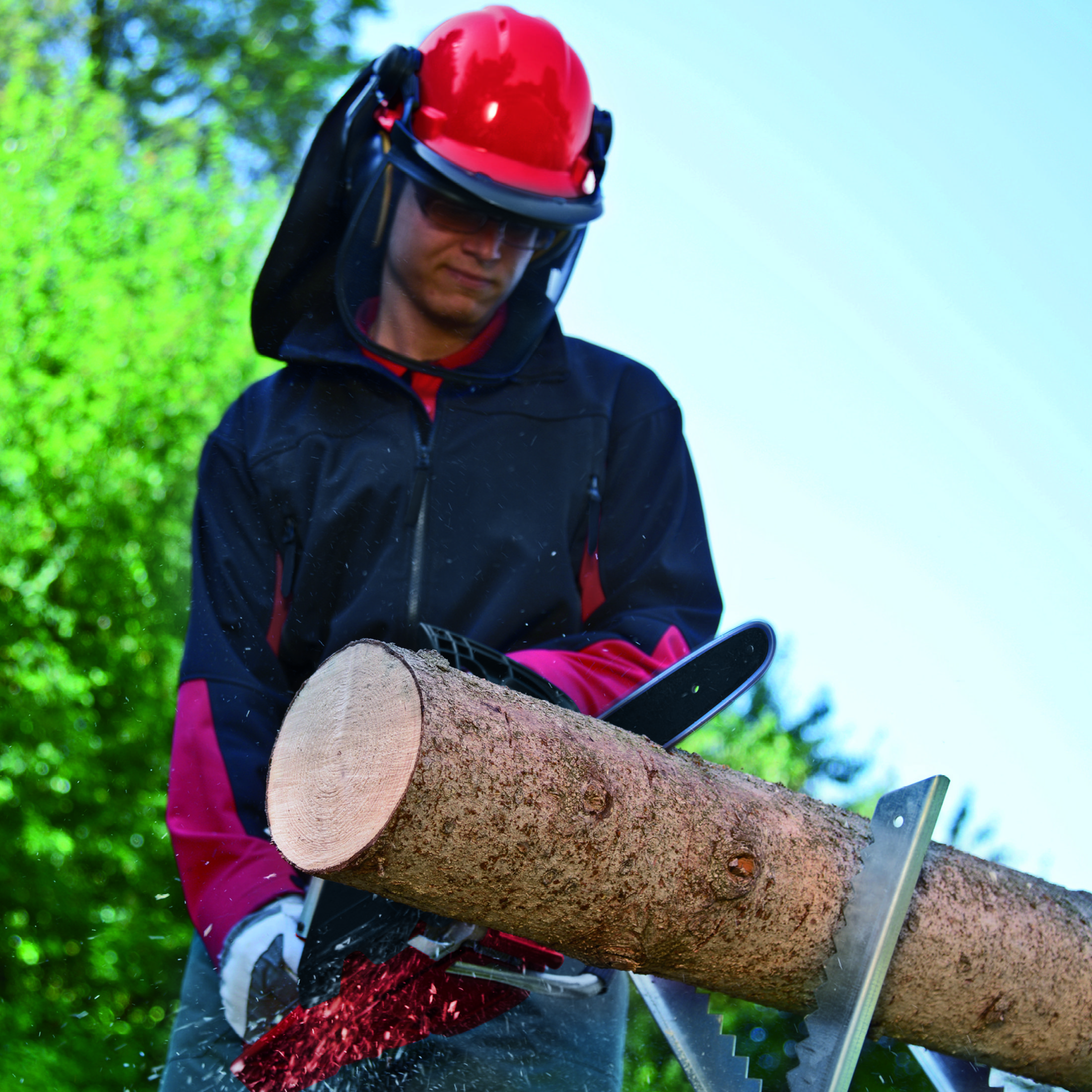 Osoba nosząca sprzęt ochronny tnie kłodę piłą łańcuchową na zewnątrz.