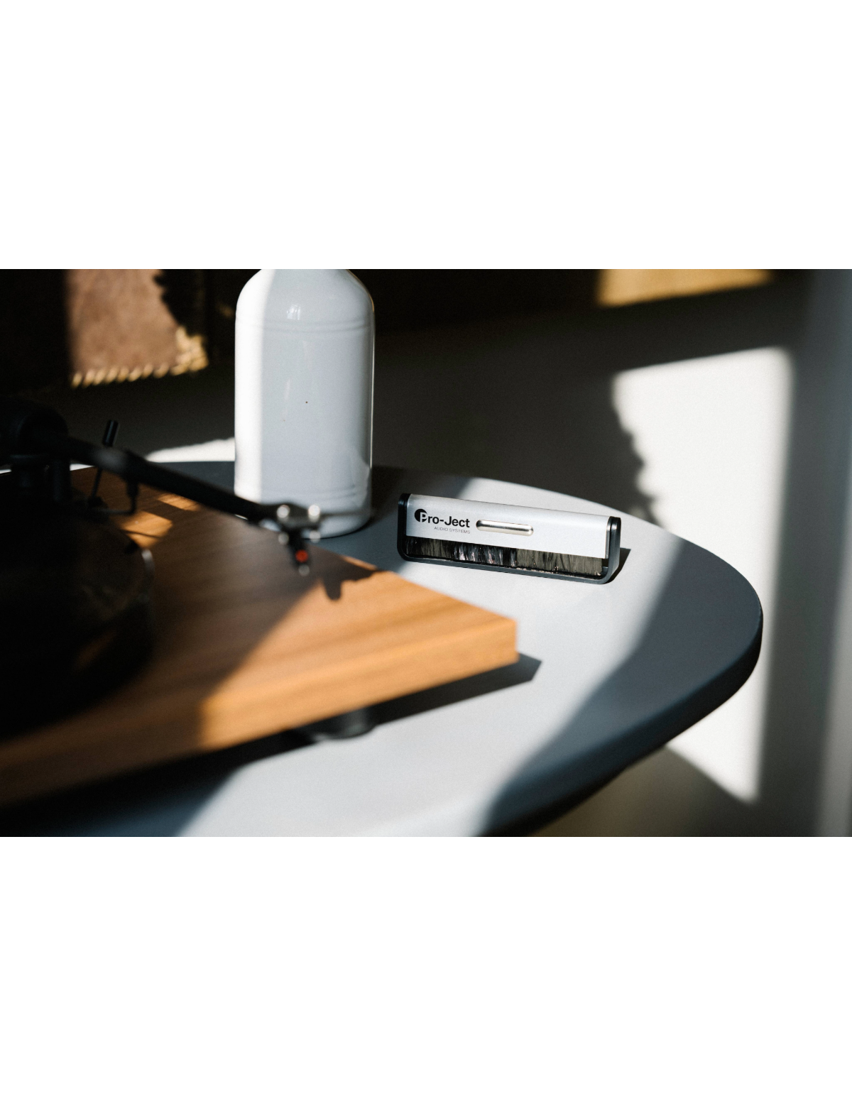 Szczotka do czyszczenia płyt i butelka na szarym stole. W tle gramofon.