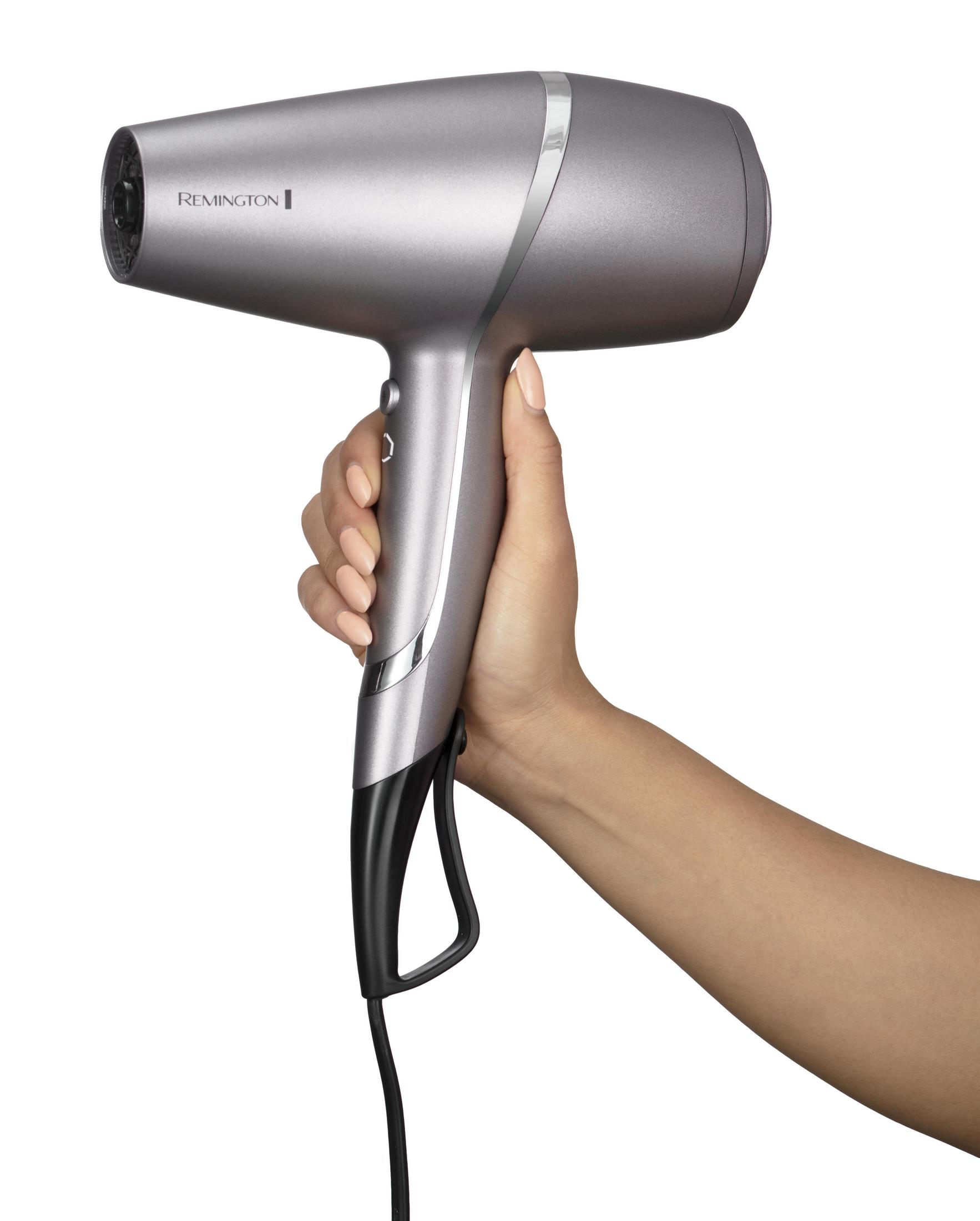 Dłoń trzymająca srebrną suszarkę Remington na białym tle.