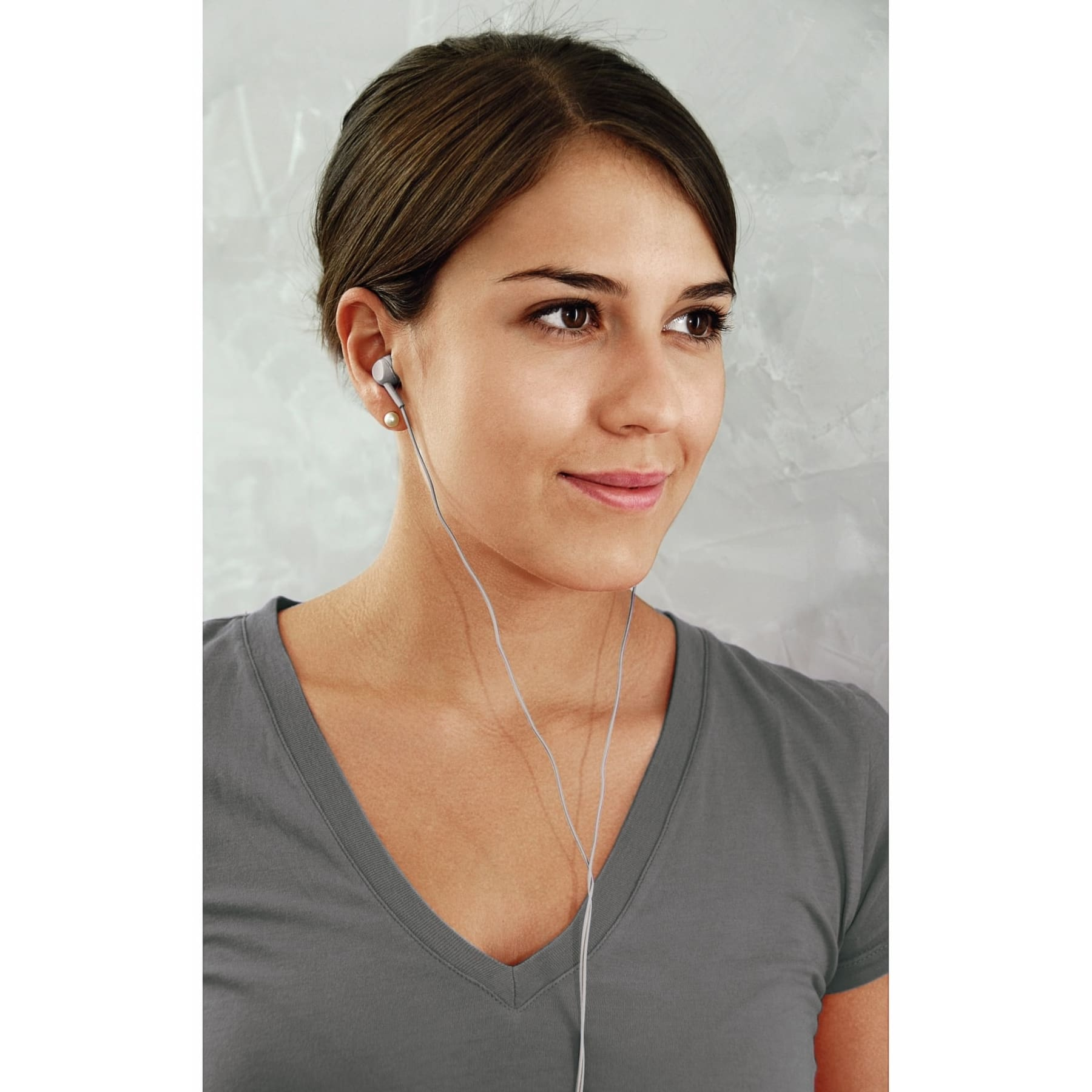 Frau mit Kopfhörern. Lächelt, schaut nach rechts. Graues T-Shirt, heller Hintergrund.