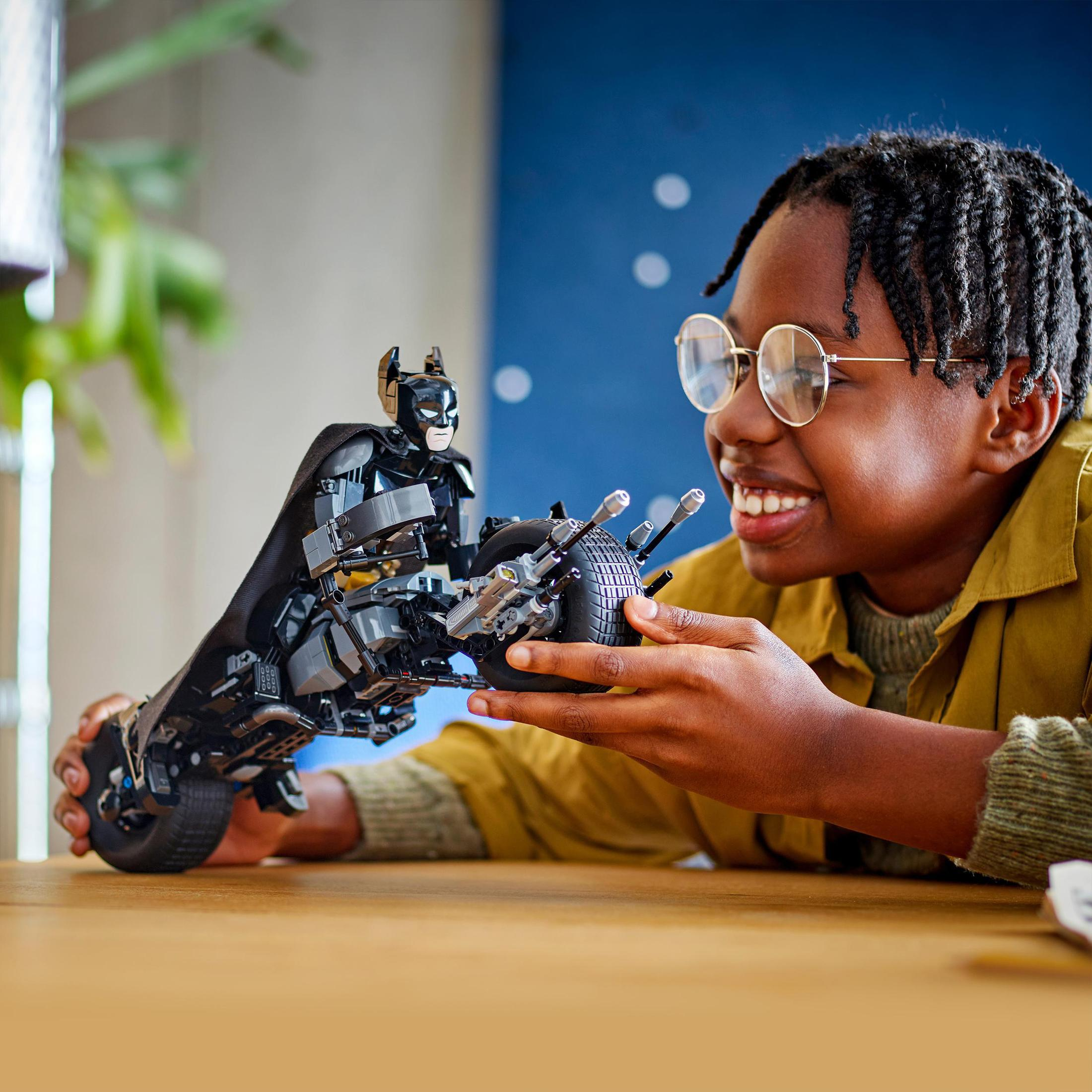 Chłopiec uśmiecha się trzymając zabawkę Lego Batmana na stole.