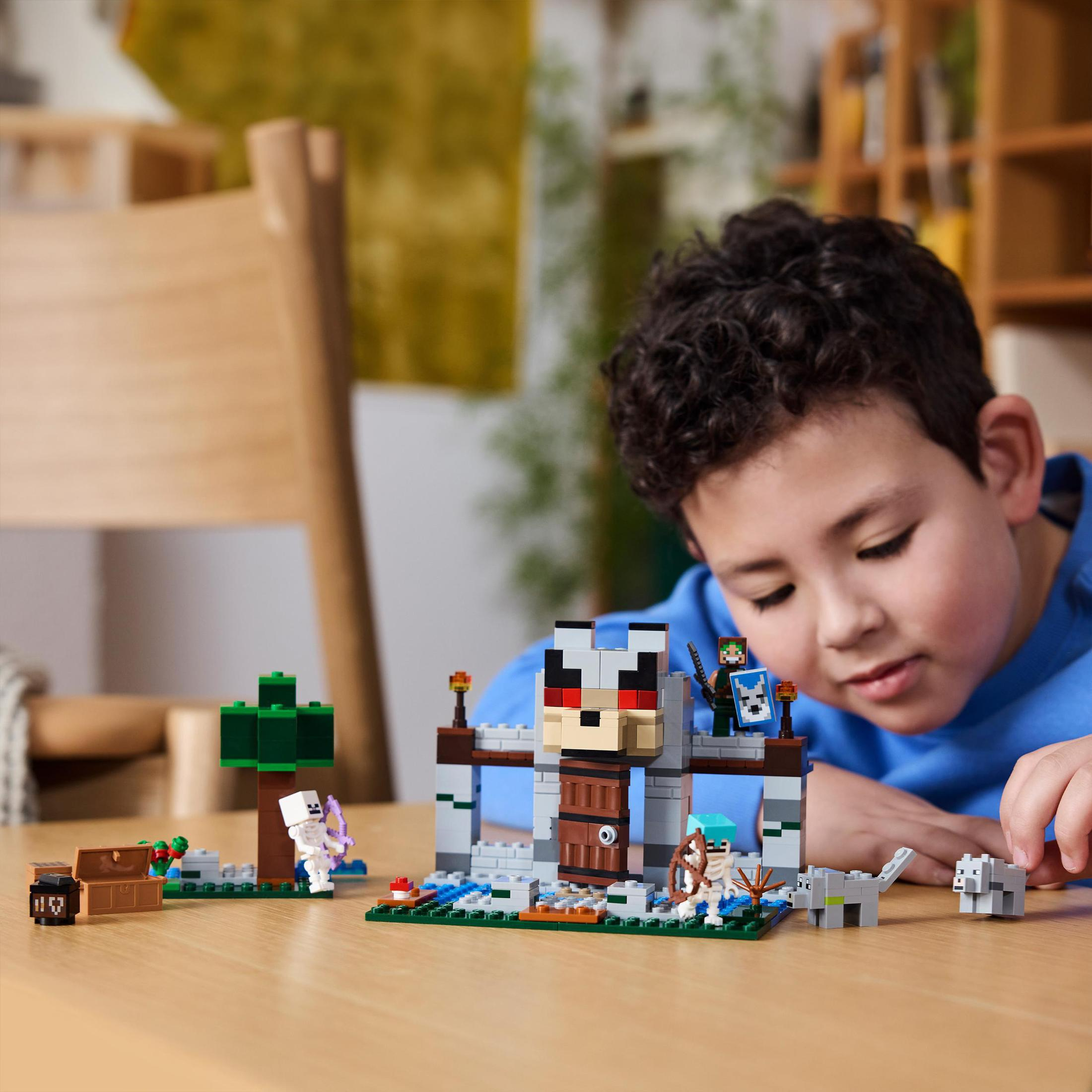 Ein Kind spielt mit einem Lego Minecraft Set. Struktur und Figuren stehen auf einem Holztisch.