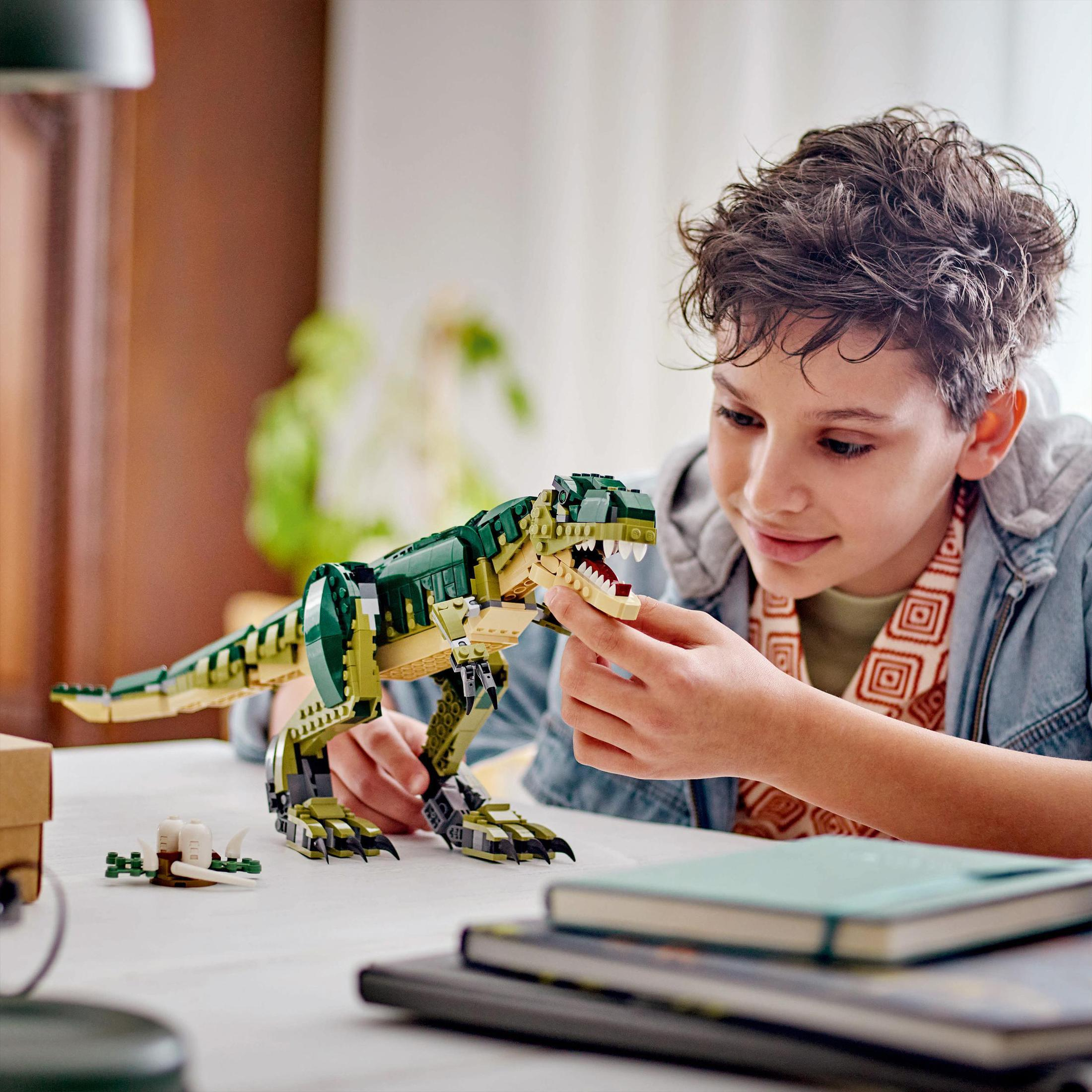 Chłopiec bawi się modelem dinozaura Lego. Model jest zielony i brązowy, a chłopiec się uśmiecha.