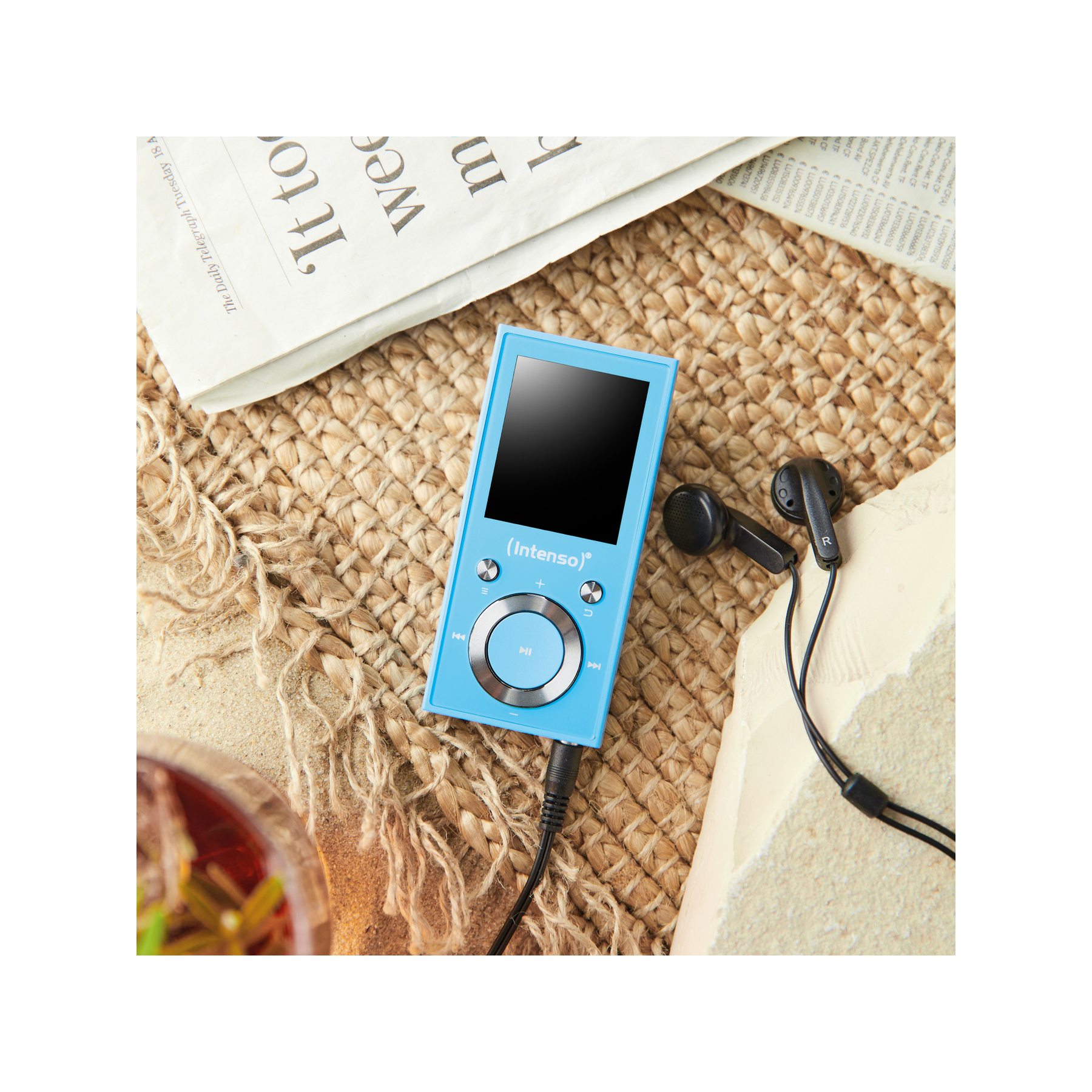 Niebieski odtwarzacz MP3 z czarnymi słuchawkami na beżowej powierzchni z gazetą w tle.