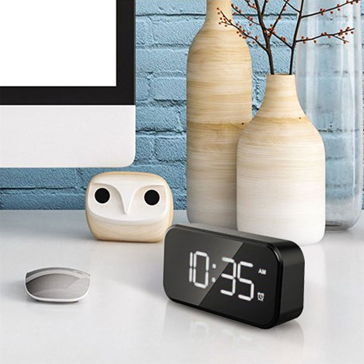 Eine schwarze Digitaluhr zeigt die Zeit an. Daneben befinden sich eine Eulenfigur und eine Computermaus.