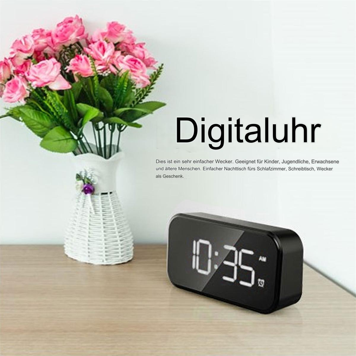 Schwarze Digitaluhr auf einem Holztisch mit Blumen in einer Vase.