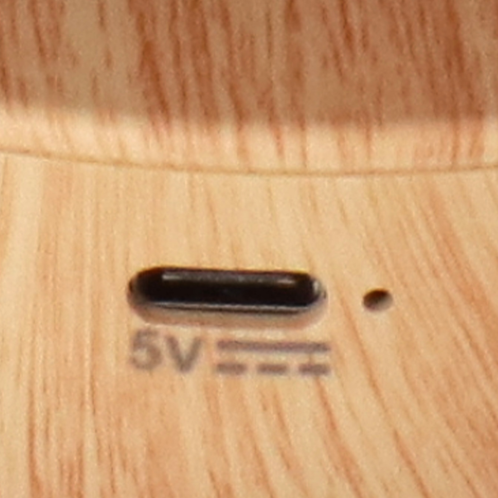 Nahaufnahme einer Holzoberfläche mit einem USB-C-Anschluss und dem Text 5V. Neben dem Anschluss befindet sich ein kleiner Punkt.